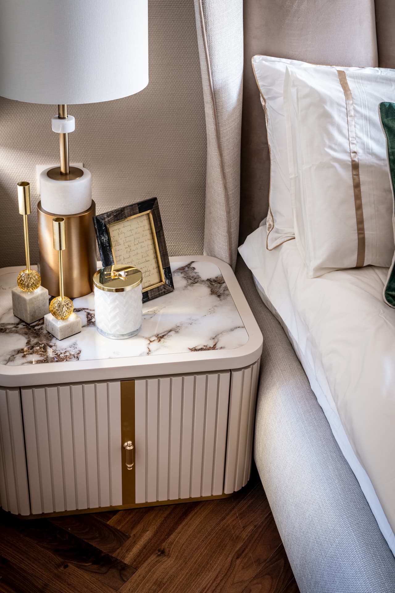 Fluted cream nightstand with a brass strip and veined stone top beside the upholstered bed in the bedroom of Cognac