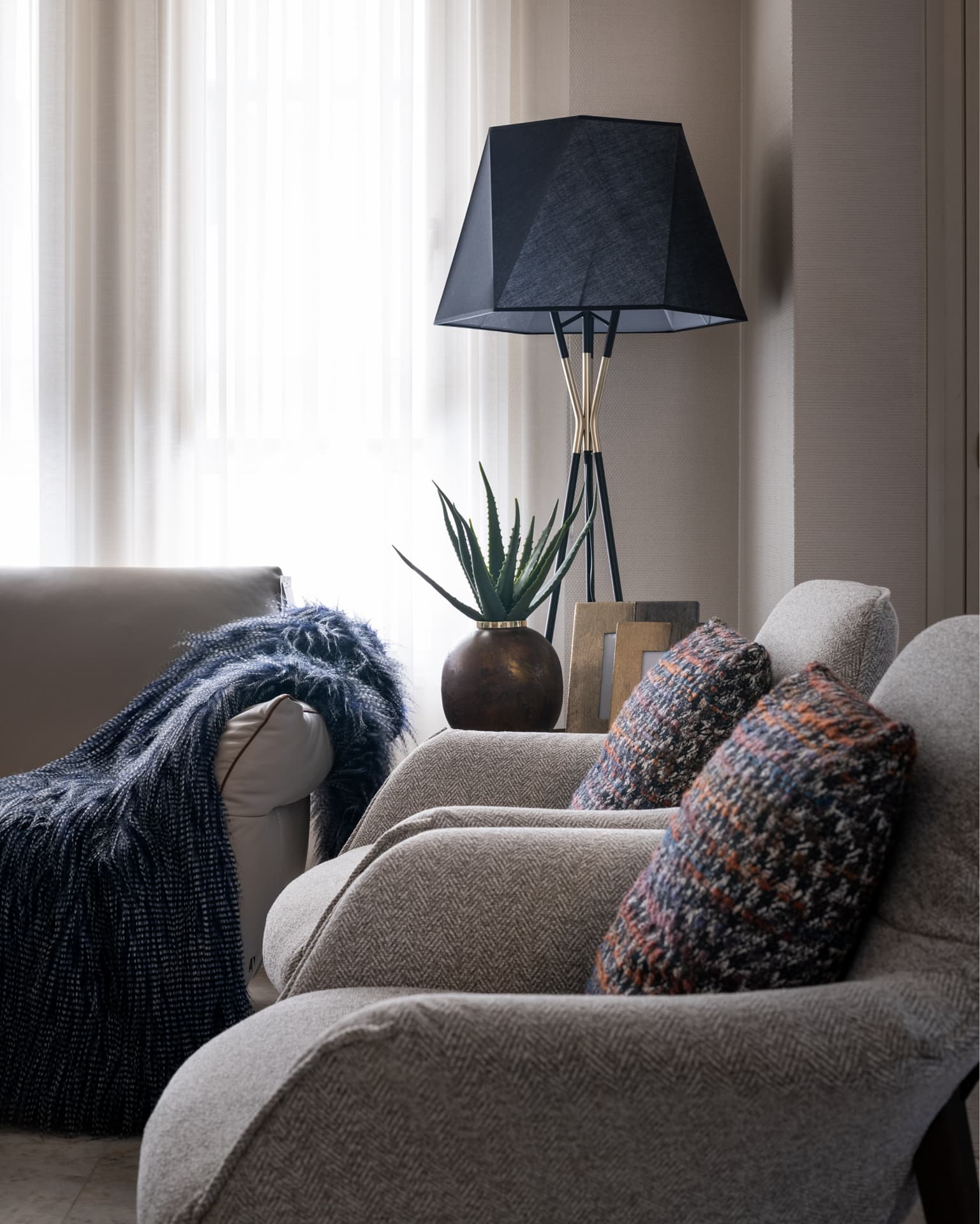 Herringbone armchairs with textured cushions beside a black faceted floor lamp and a shaggy navy throw in the salon of Cognac