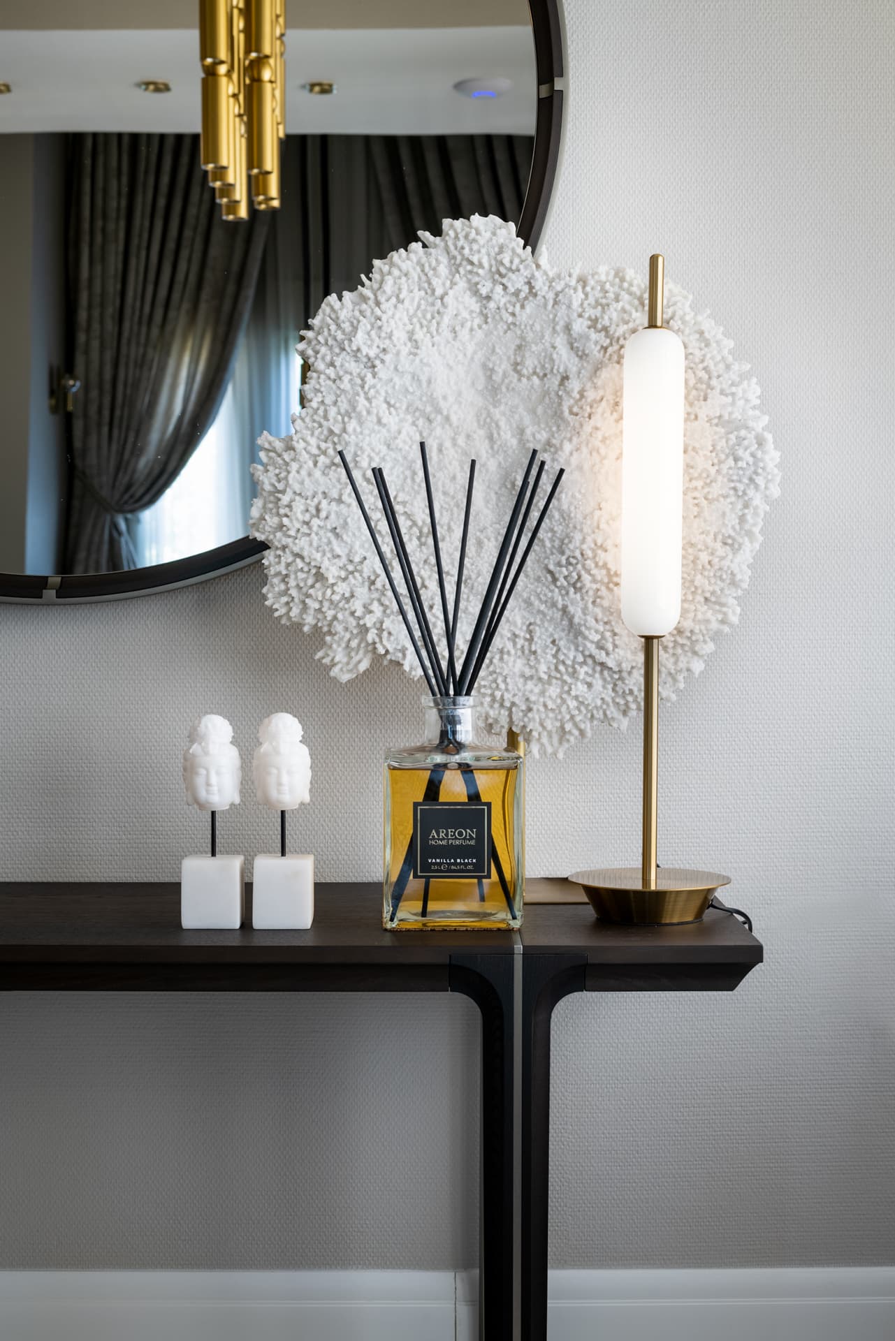 White coral-like sculpture, a brass tube table lamp and small white busts on a dark console before a round mirror in the salon of Cognac
