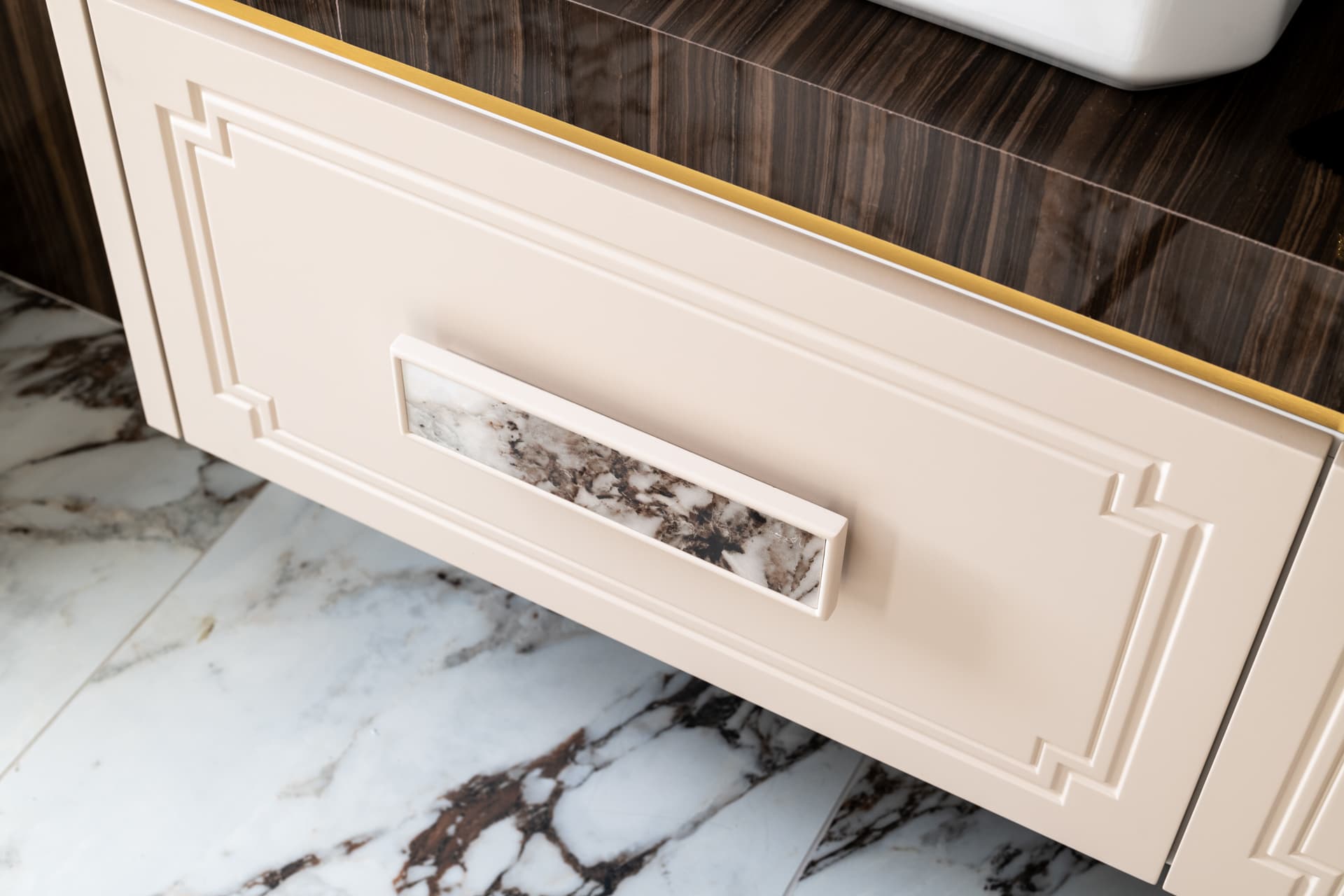 Close-up of a cream vanity drawer with a veined stone-inlay pull and a brass trim line in the master bathroom of Cognac