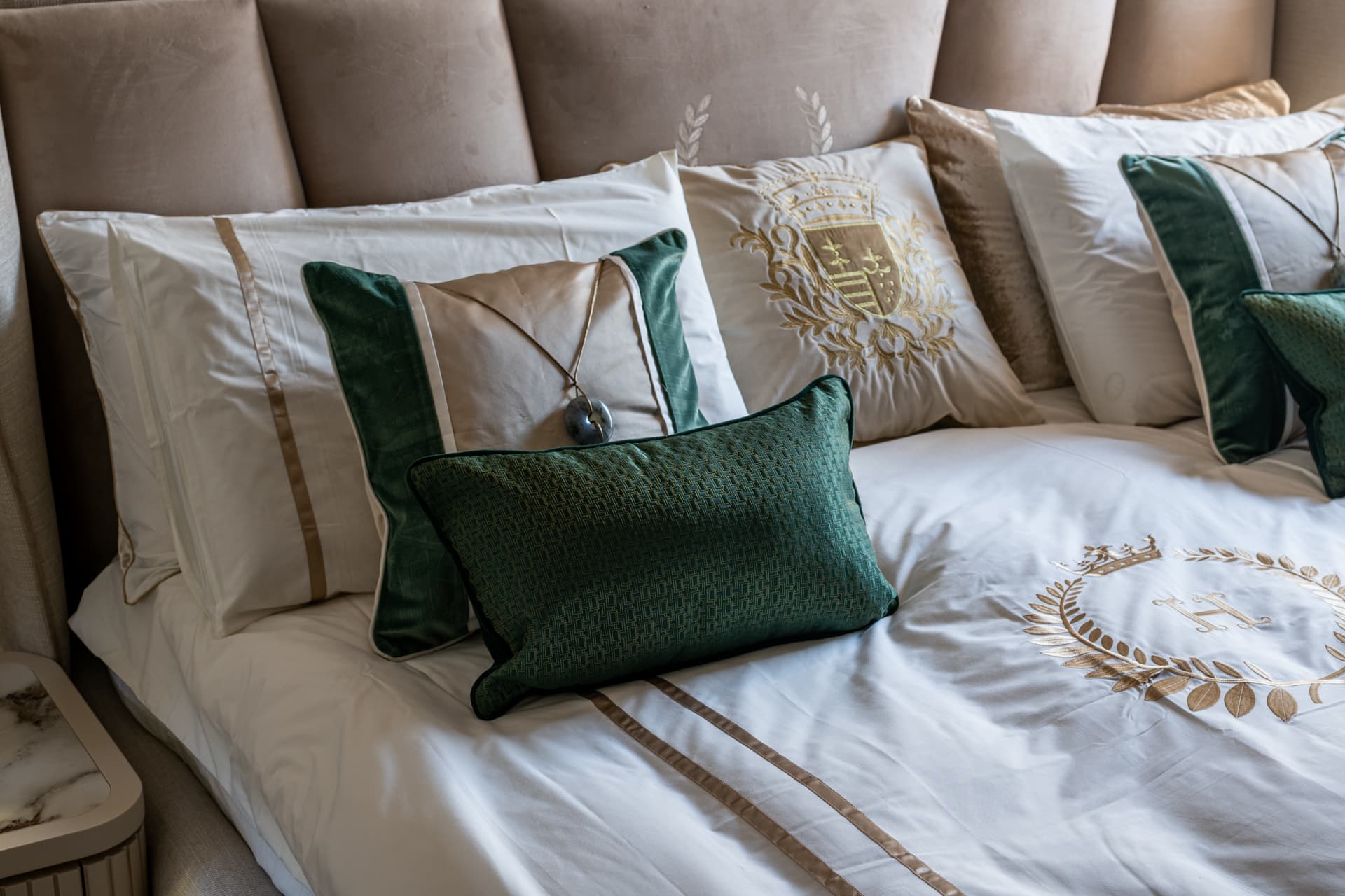 Gold-embroidered white bedding with striped pillows and green velvet cushions against the tufted headboard in the bedroom of Cognac