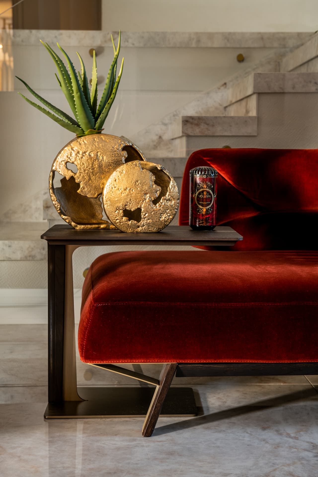 Hammered brass globe planters on a side table by the rust velvet sofa, stone staircase behind, in the living room of Cognac
