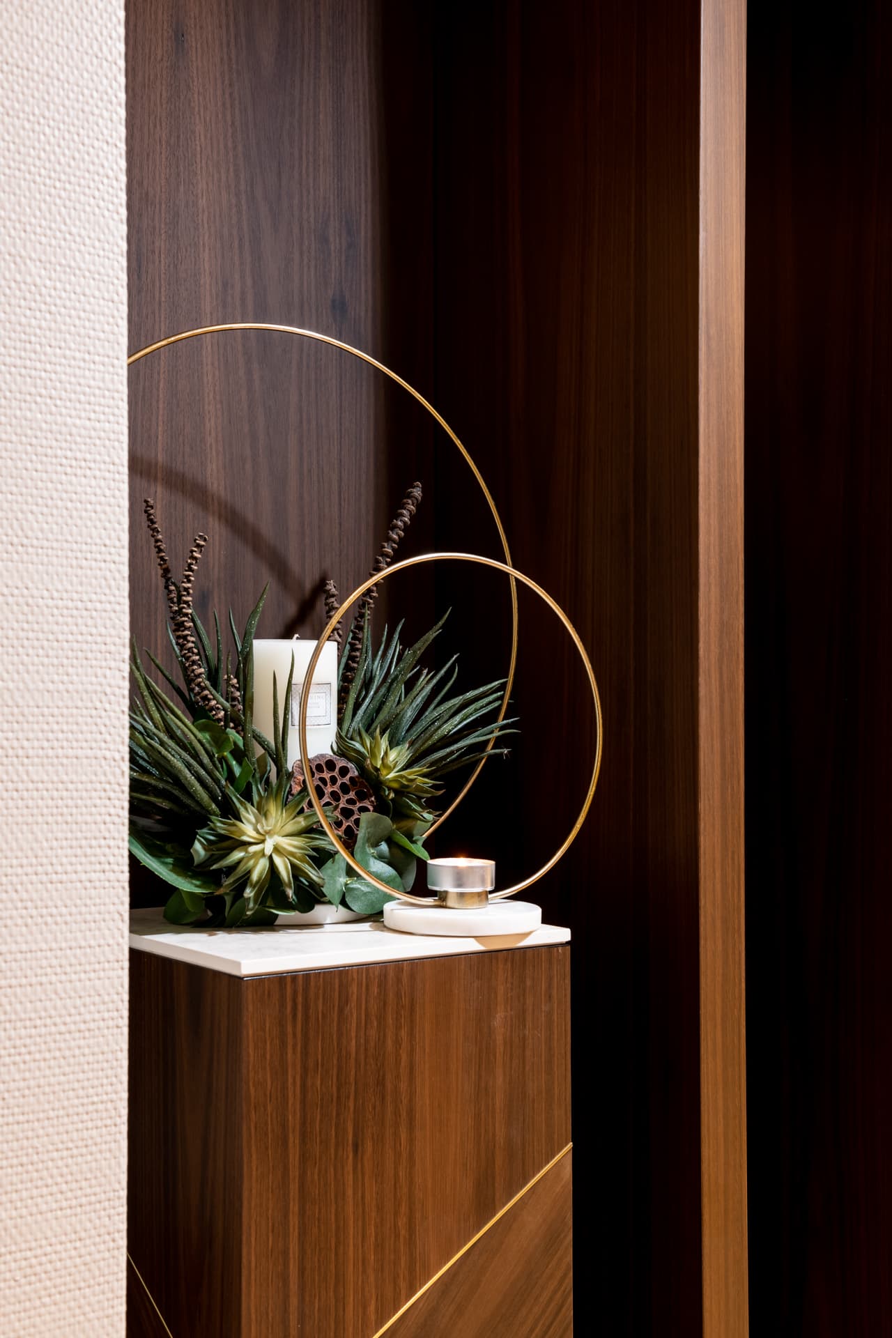 Brass ring candle holders and succulents on a stone-topped walnut plinth with brass inlay at the kitchen entry of Cognac