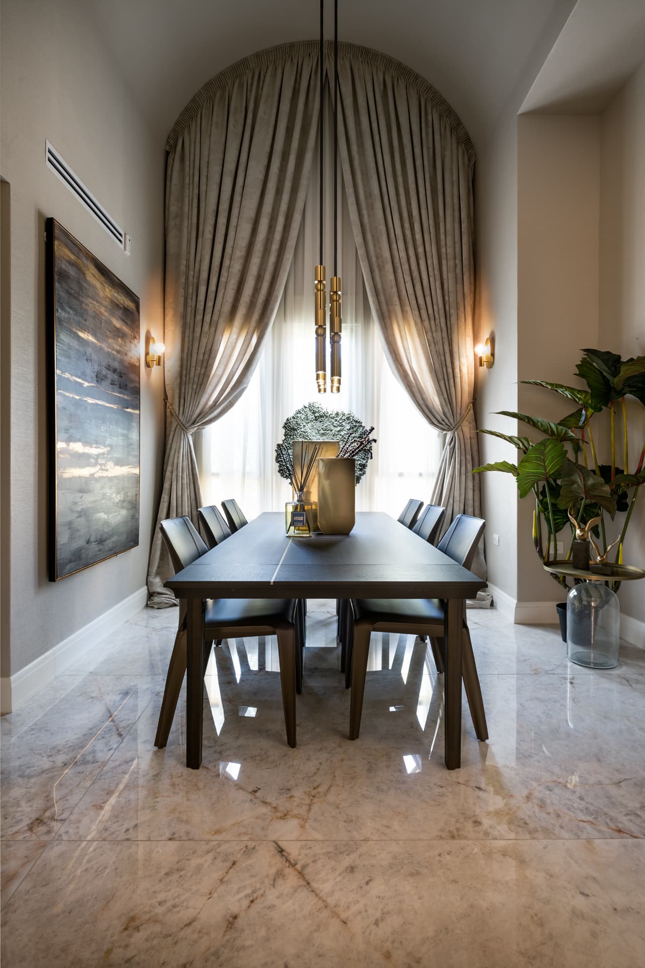 Dining room with a dark wood table and leather chairs before an arched, floor-length curtained window under a brass pendant in Cognac