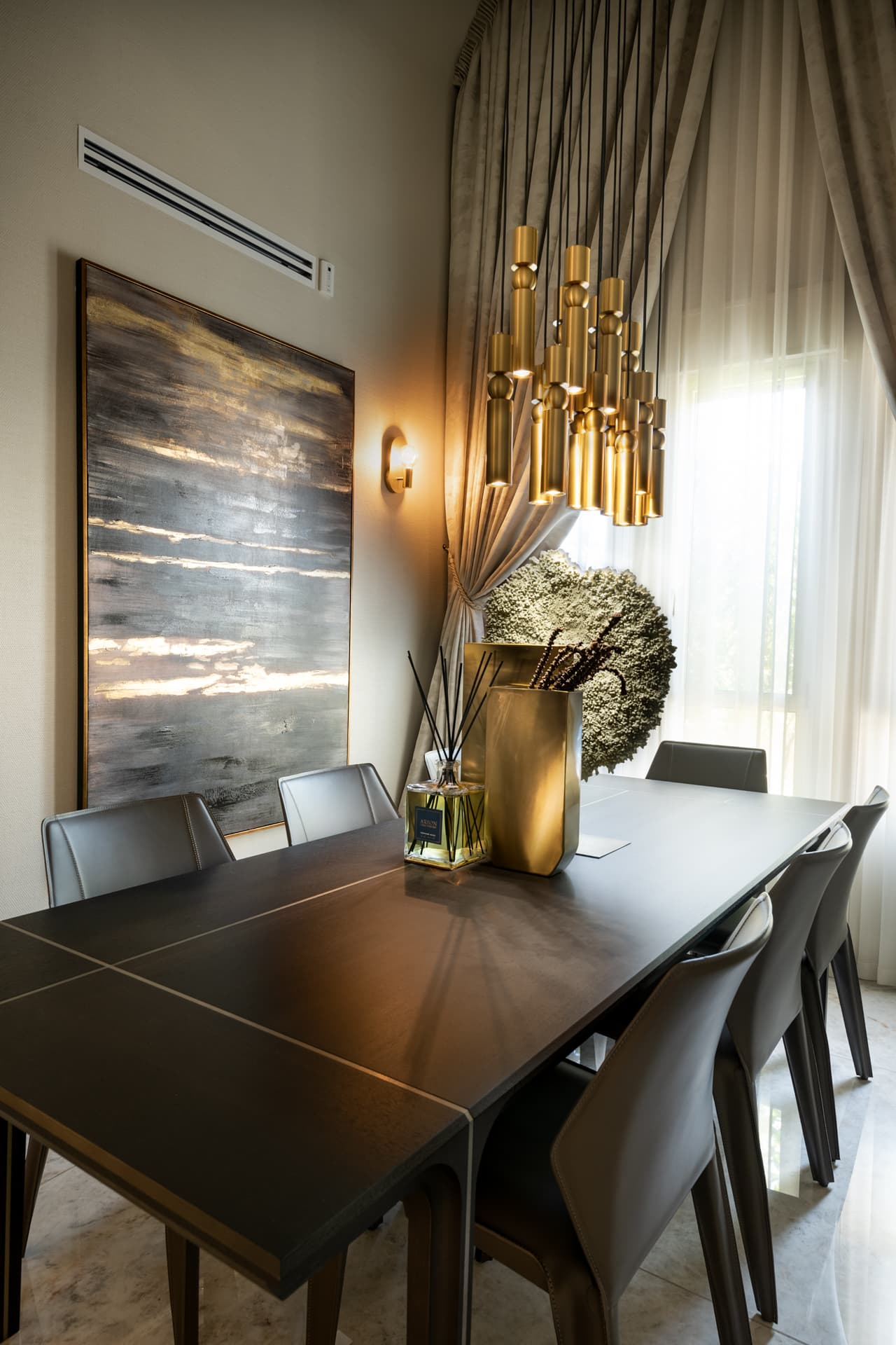 Angled view of the dark wood dining table under clustered brass tube pendants beside a large abstract painting in the dining room of Cognac