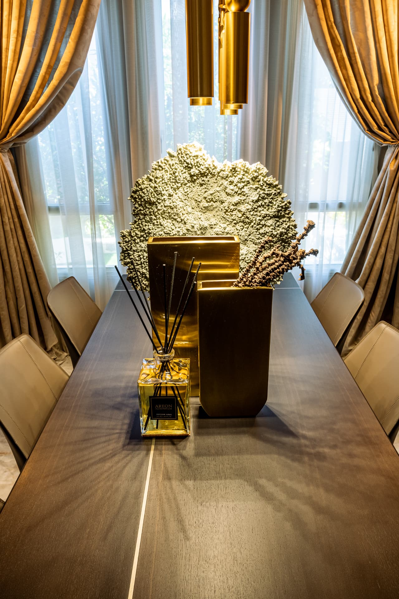 Brass vases and a sculptural coral-like centrepiece on the dark wood table, framed by tied-back curtains, in the dining room of Cognac