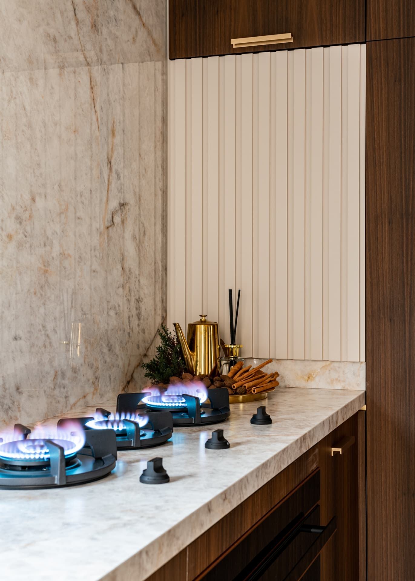 Gas hob on a veined stone counter against a stone backsplash and a fluted cream panel with walnut cabinets in the kitchen of Cognac