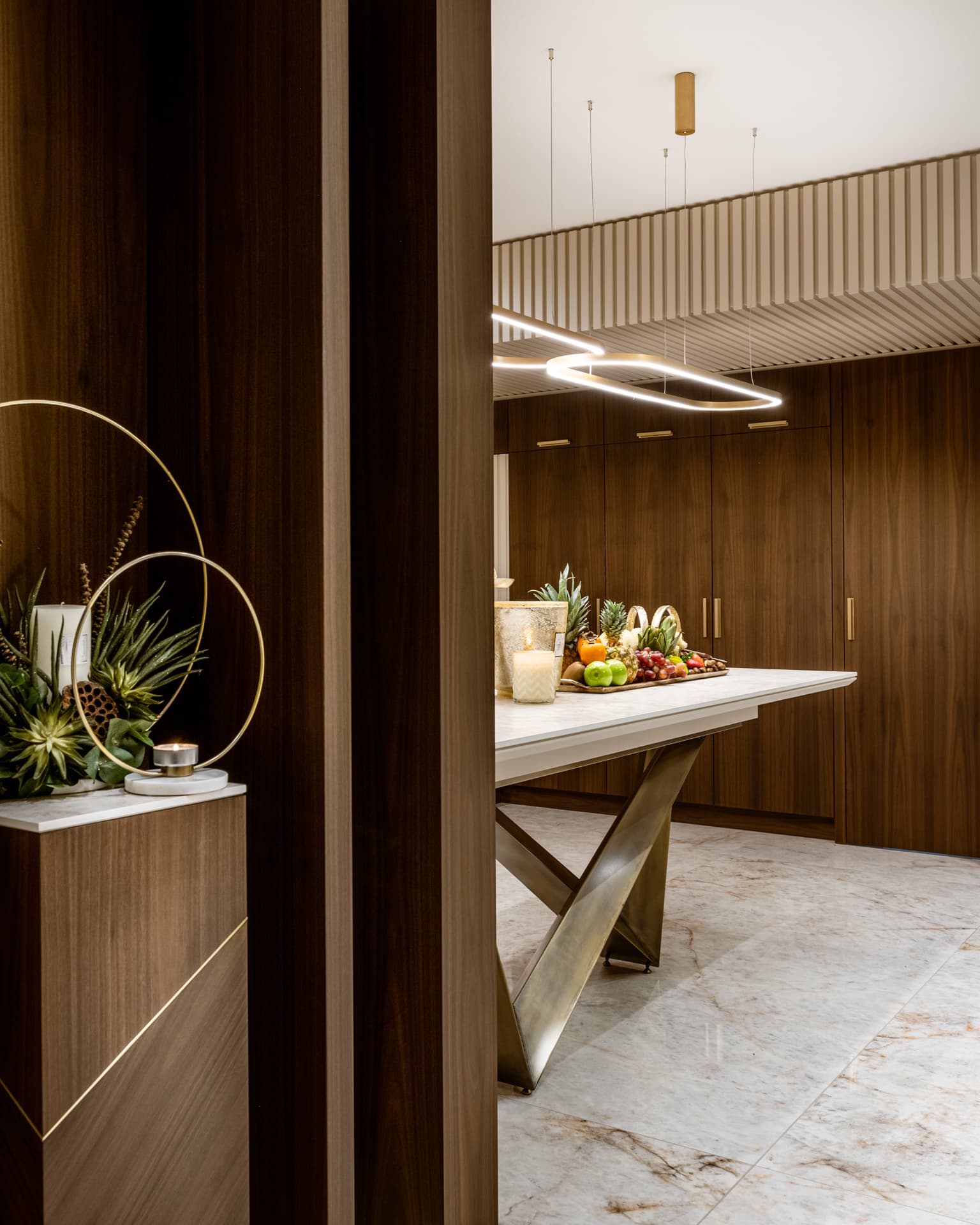 Walnut-clad passage opening onto the kitchen, with a stone table on bronze legs and floor-to-ceiling walnut cabinetry, in Cognac