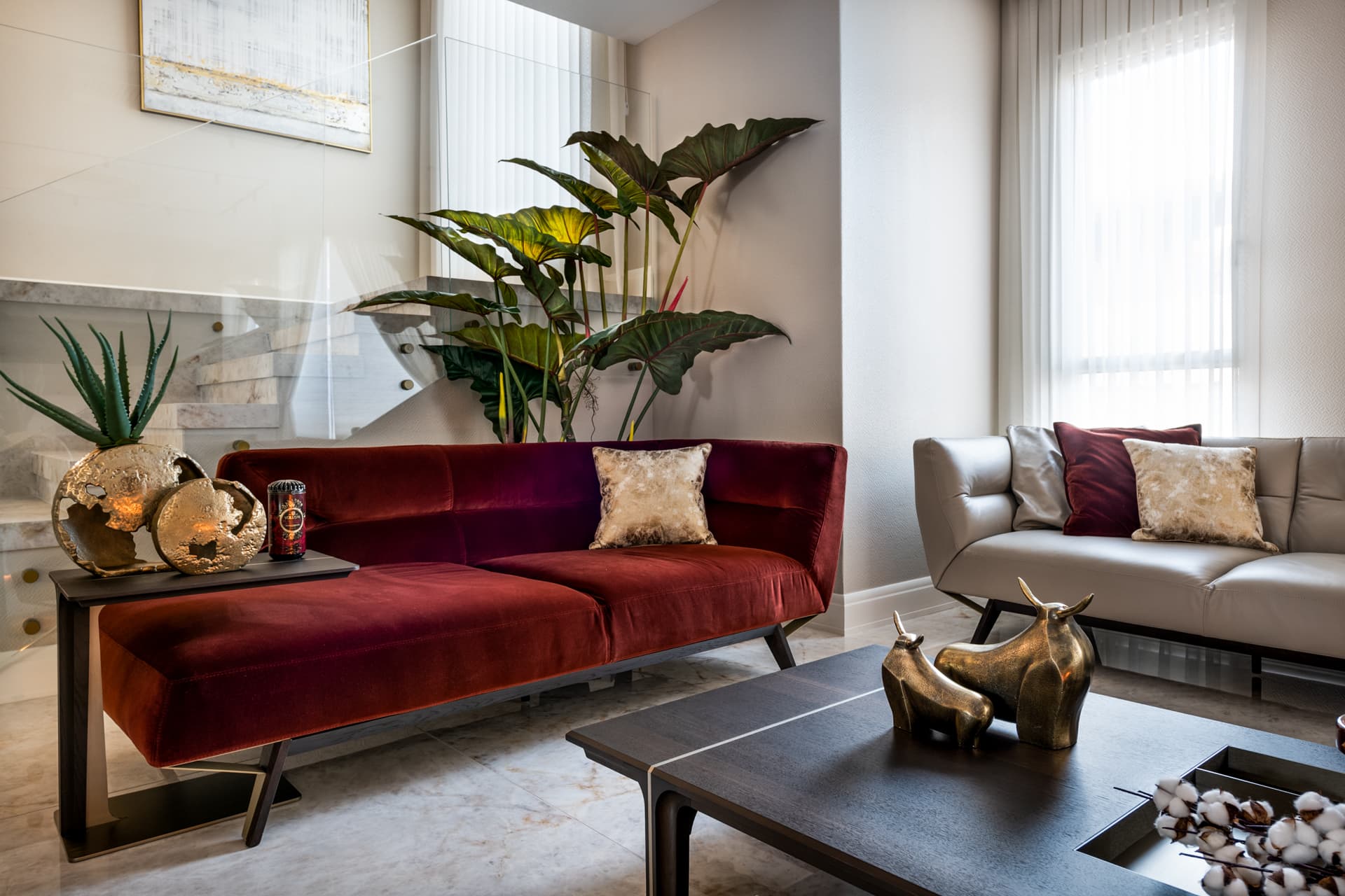 Rust velvet sofa beside a glass-railed stone staircase, with brass bull sculptures on the coffee table in the living room of Cognac