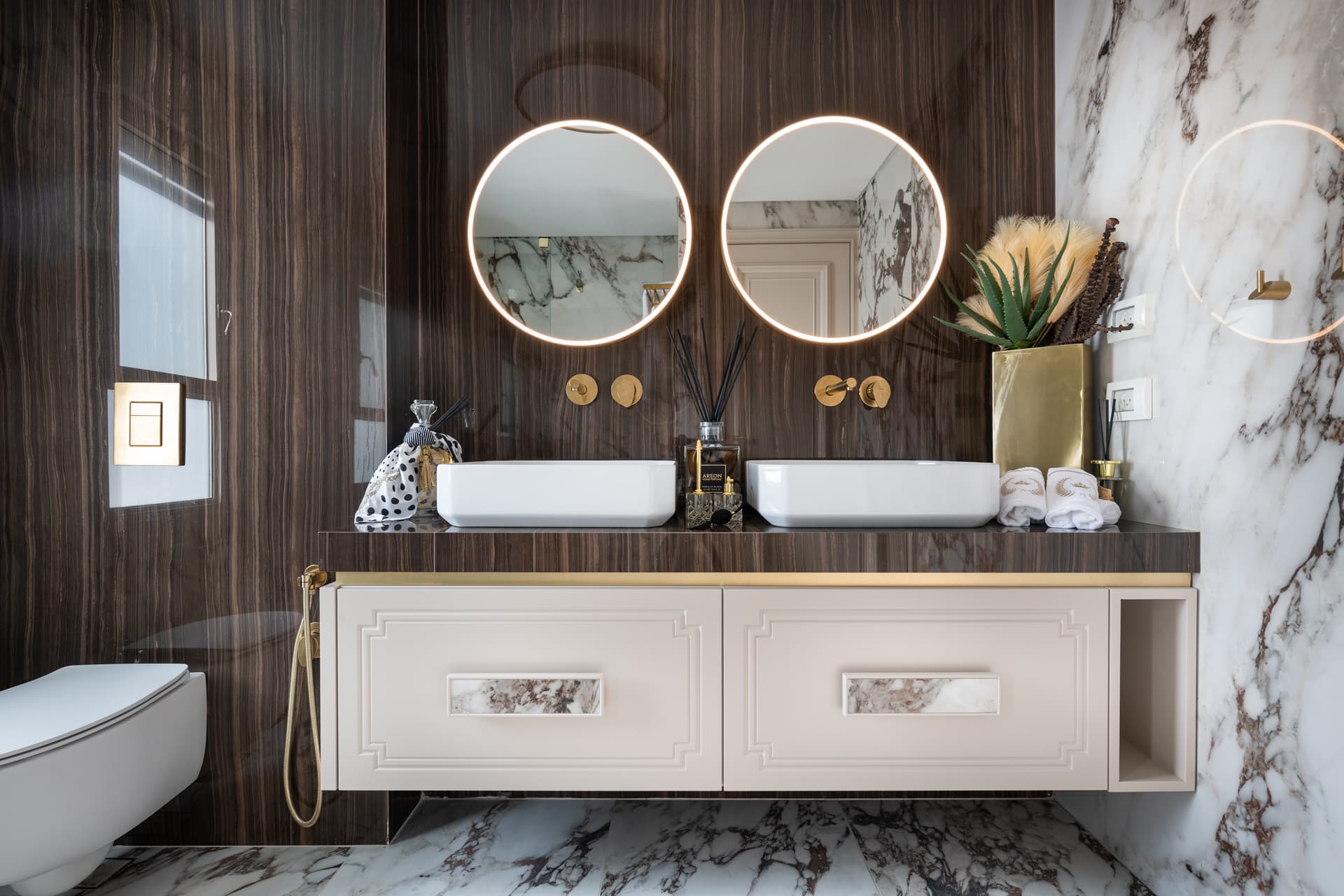 Floating cream vanity with twin vessel basins and two backlit round mirrors on a dark wood-grain wall in the master bathroom of Cognac