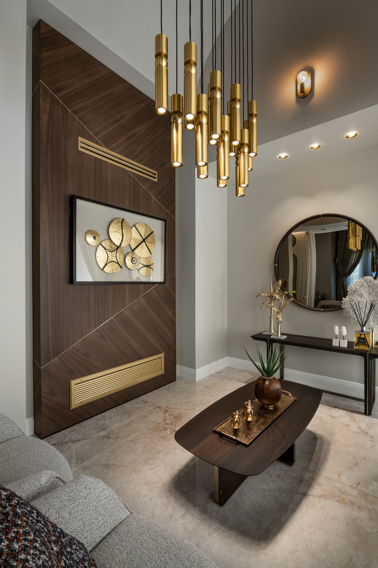 Cluster of brass tube pendants beside a walnut wall panel with brass inlay lines and a round mirror over a console in the salon of Cognac