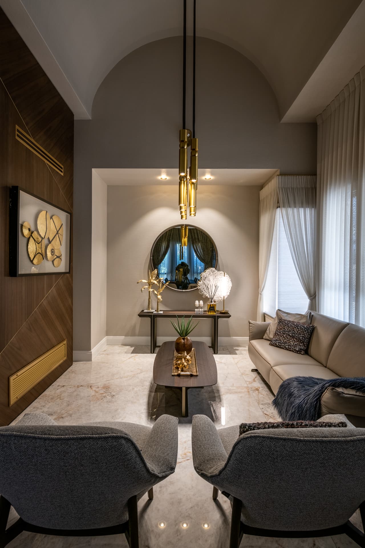 Grey armchairs facing a walnut coffee table under a vaulted ceiling and a slim brass pendant in the salon of Cognac