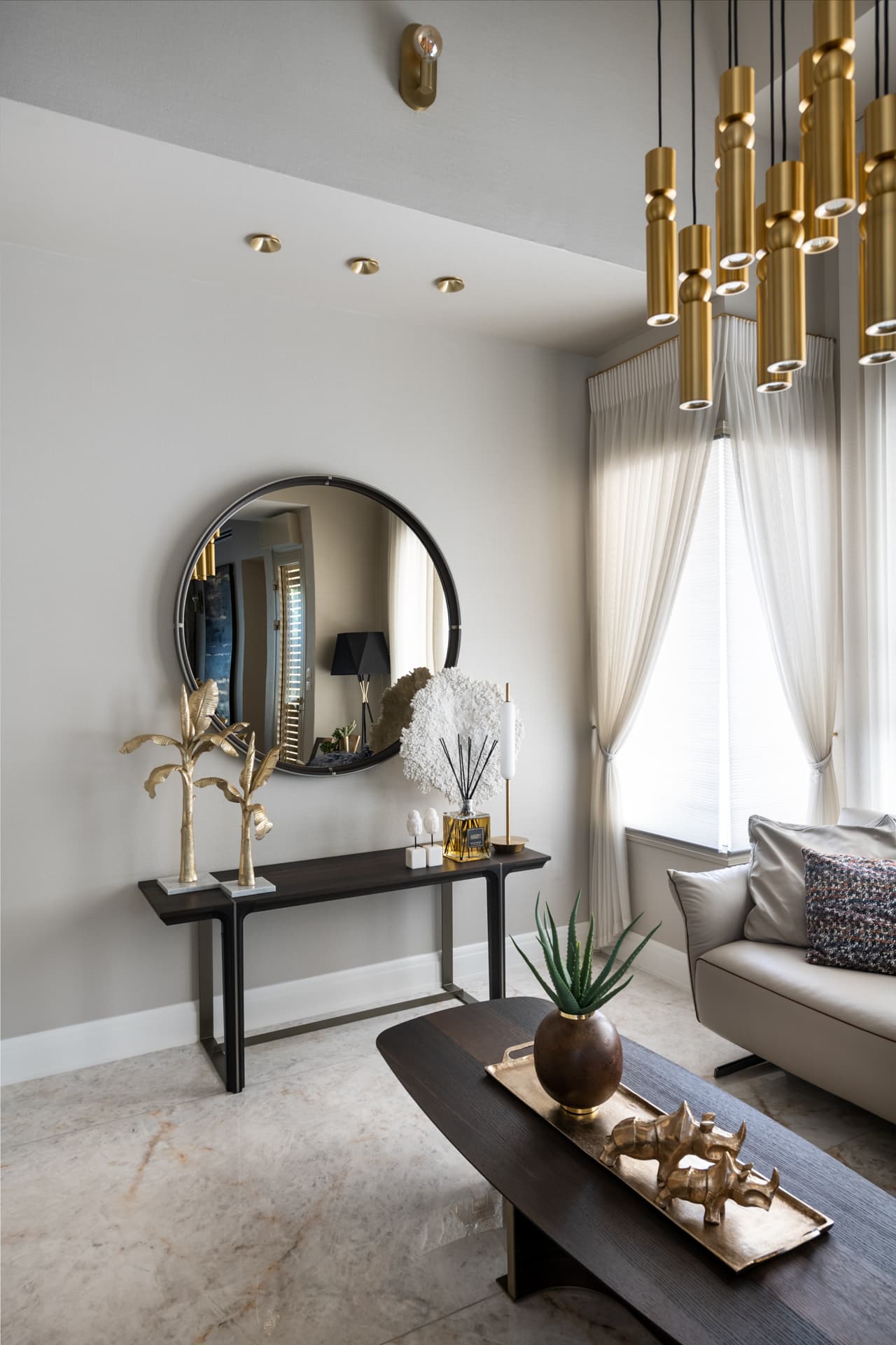 Round black-framed mirror above a slender console with brass palm sculptures, brass tube pendants hanging at right, in the salon of Cognac