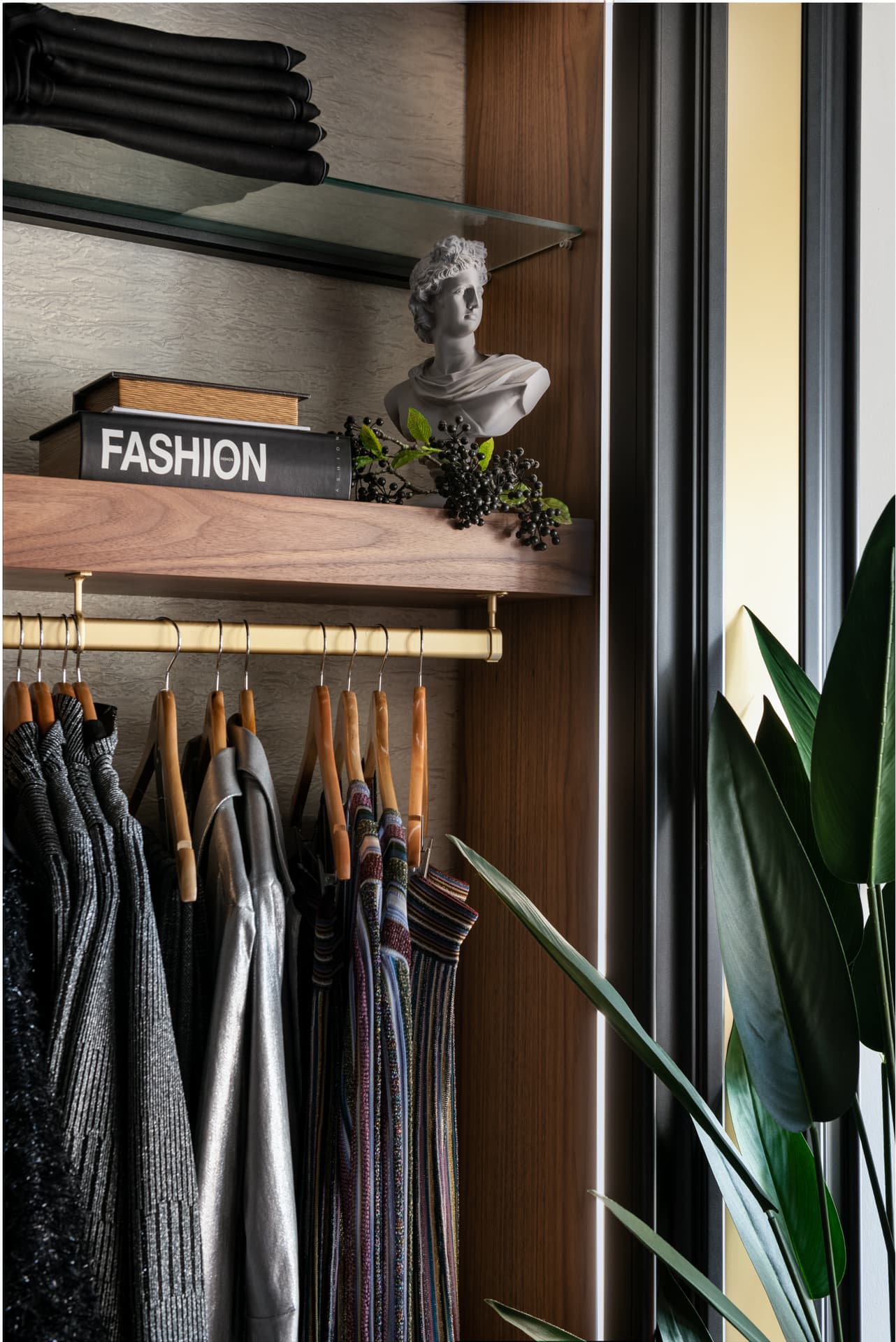 Small classical bust on a walnut shelf above a brass hanging rail with wooden hangers, inside a black-edged wardrobe niche of DxVogue