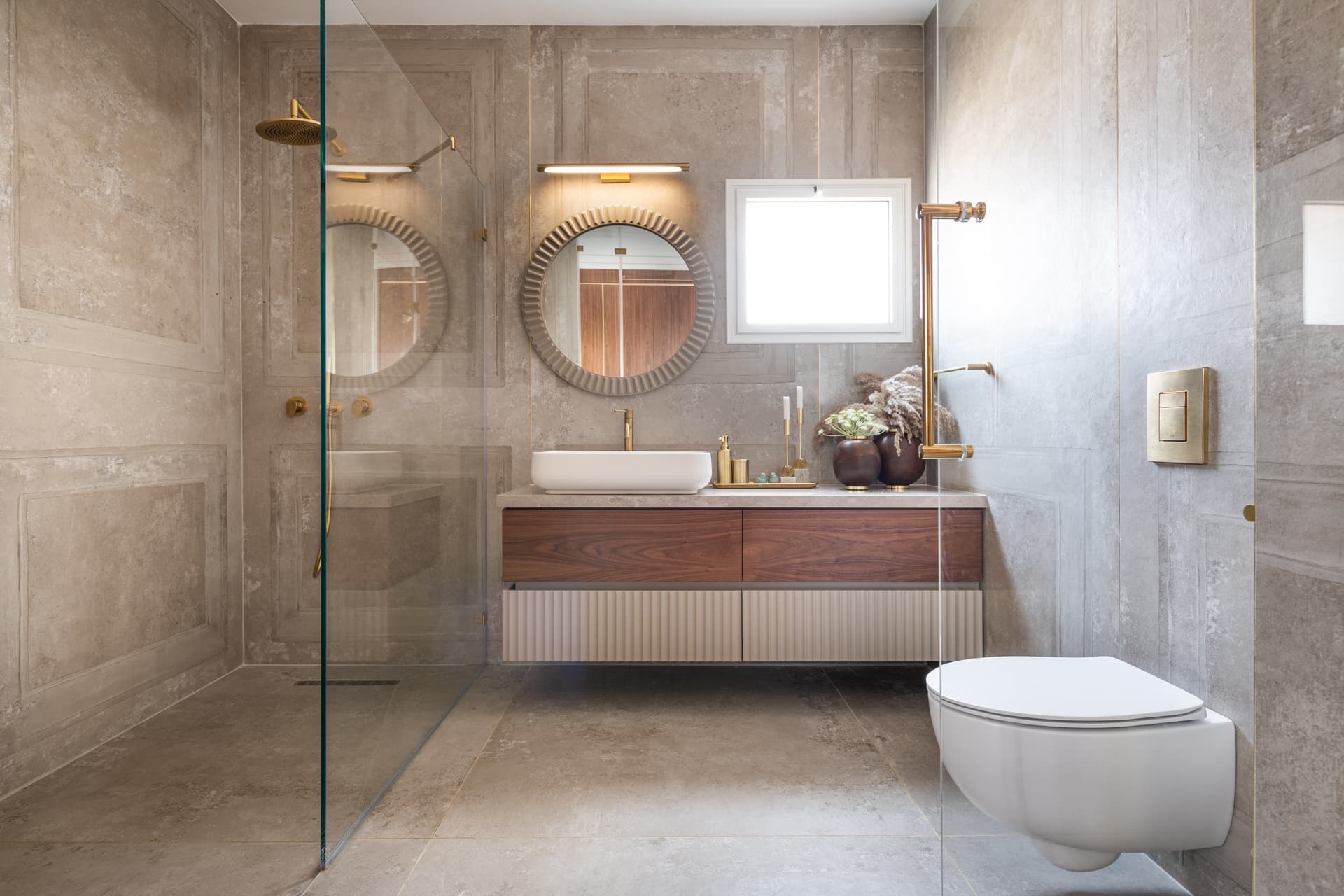 Walk-in shower, floating walnut vanity and fluted round mirror against panel-molded beige walls in the bathroom of Emperador Dark