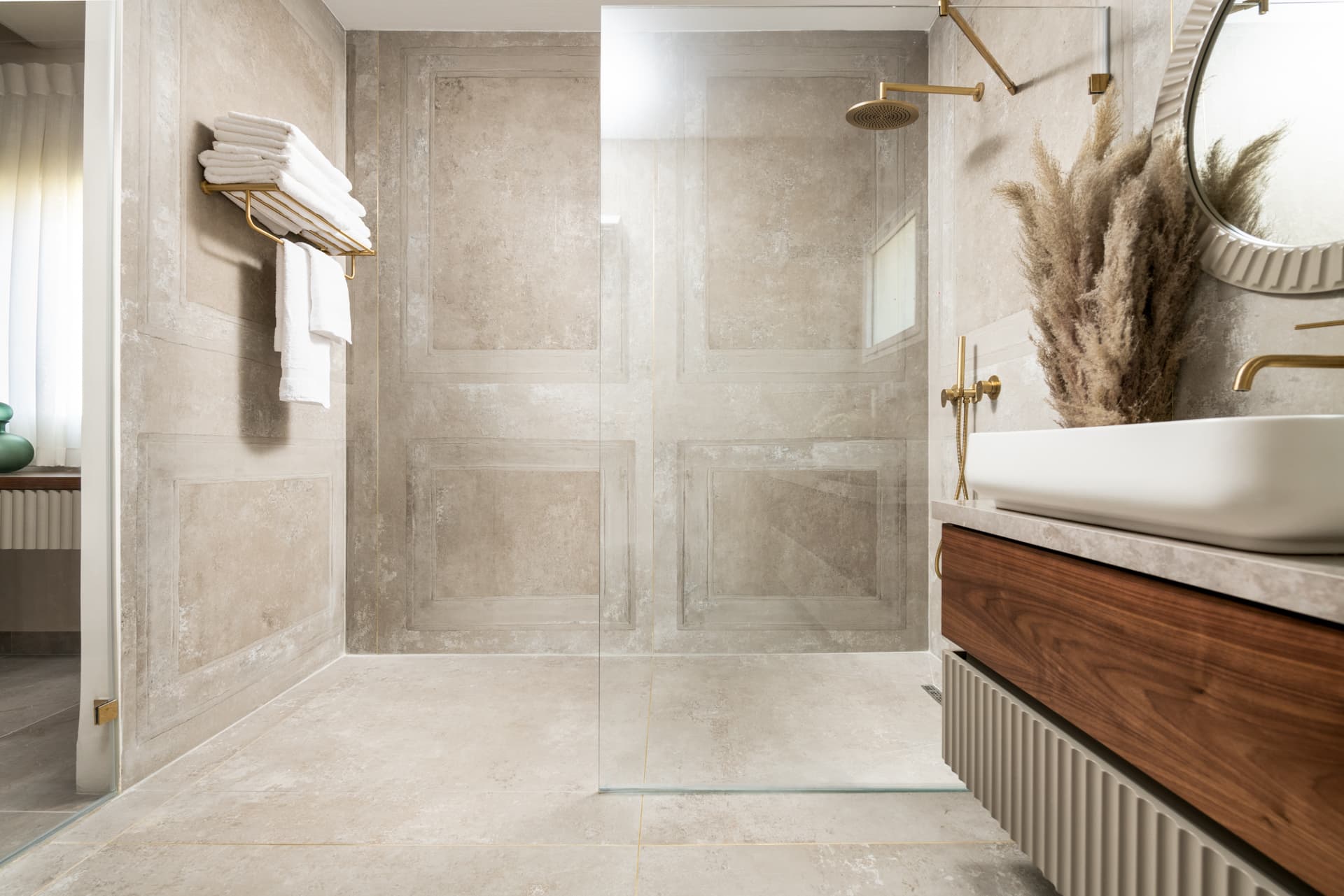 Frameless glass shower with a brass rain head and a brass towel shelf on panel-molded beige walls in the bathroom of Emperador Dark