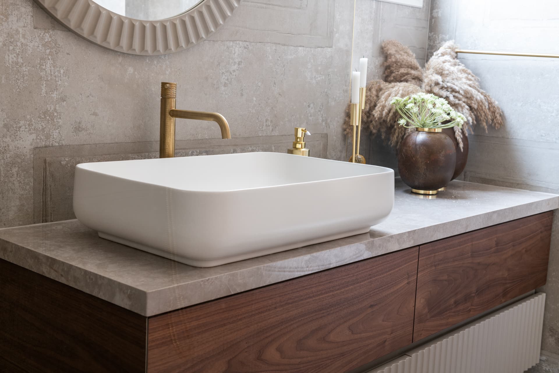 White vessel sink with a brass faucet on a grey stone top over a walnut vanity in the bathroom of Emperador Dark