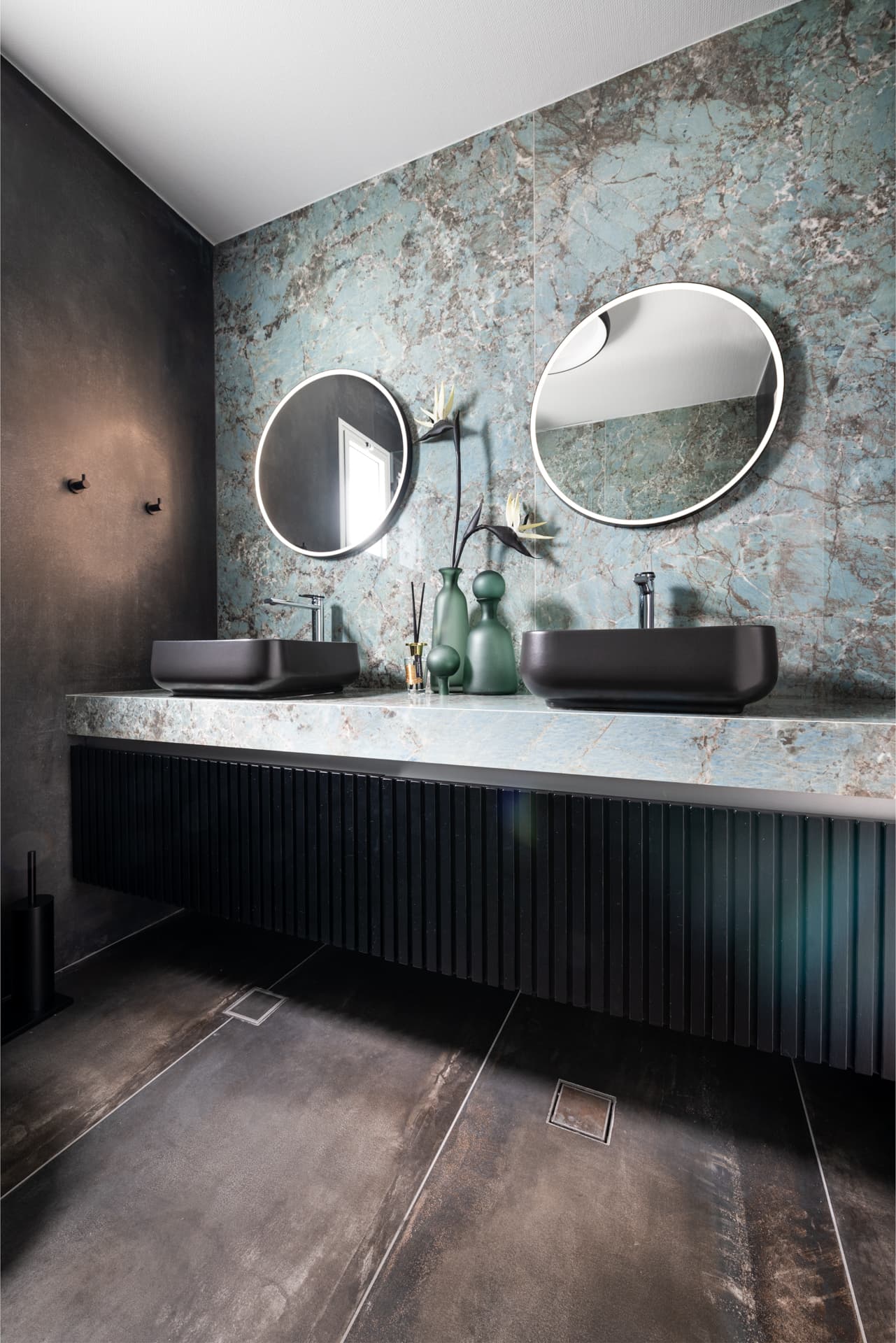 Double black vessel sinks under backlit round mirrors on a blue-green veined stone counter in the bathroom of Emperador Dark