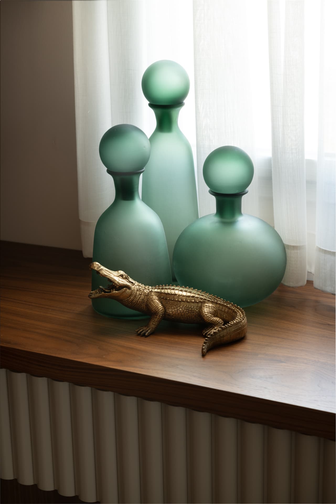 Frosted green glass bottles and a gold crocodile figurine on a walnut vanity top in the master bedroom of Emperador Dark