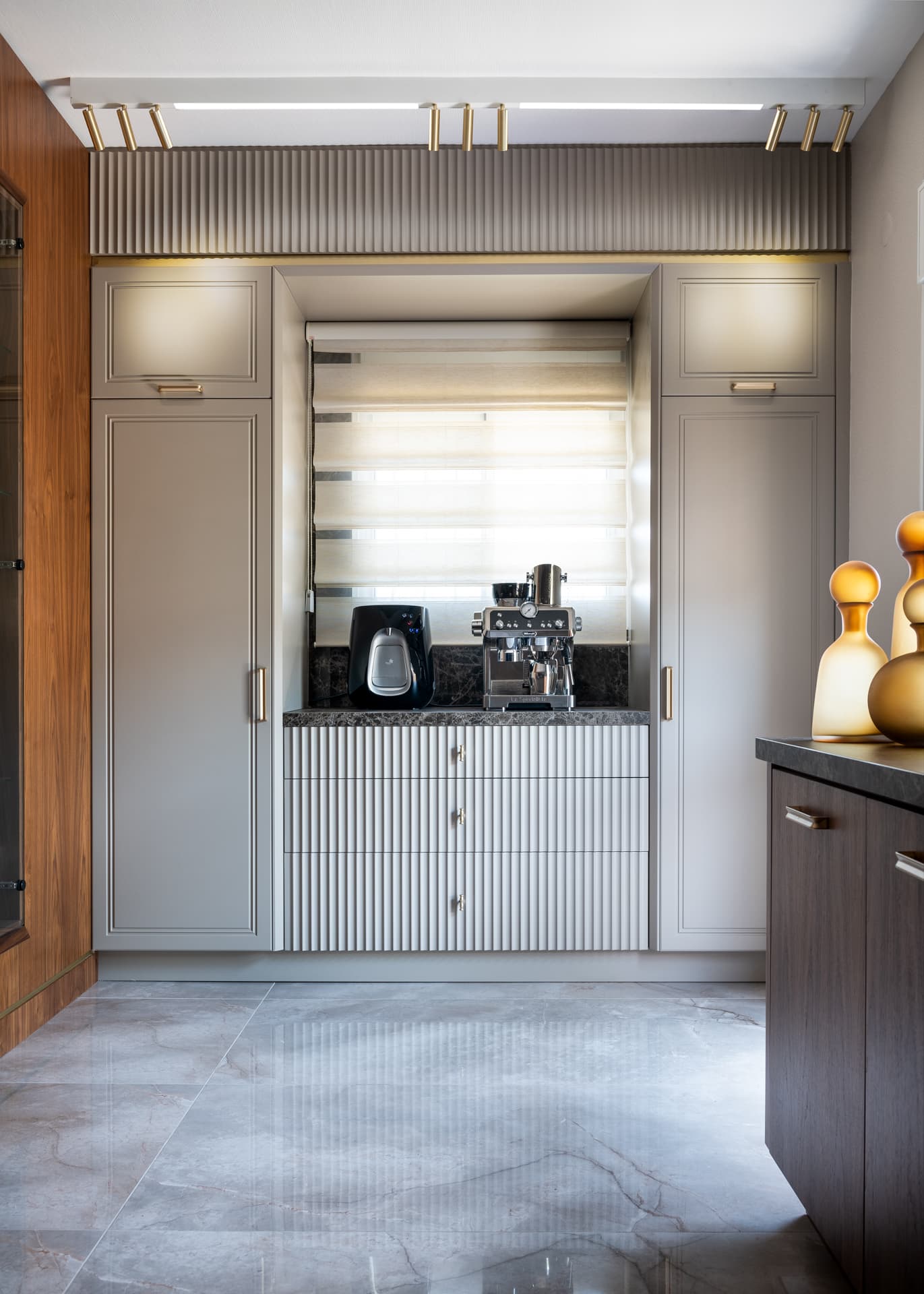 Coffee station with fluted drawers and an espresso machine set between tall grey cabinets in the kitchen of Emperador Dark