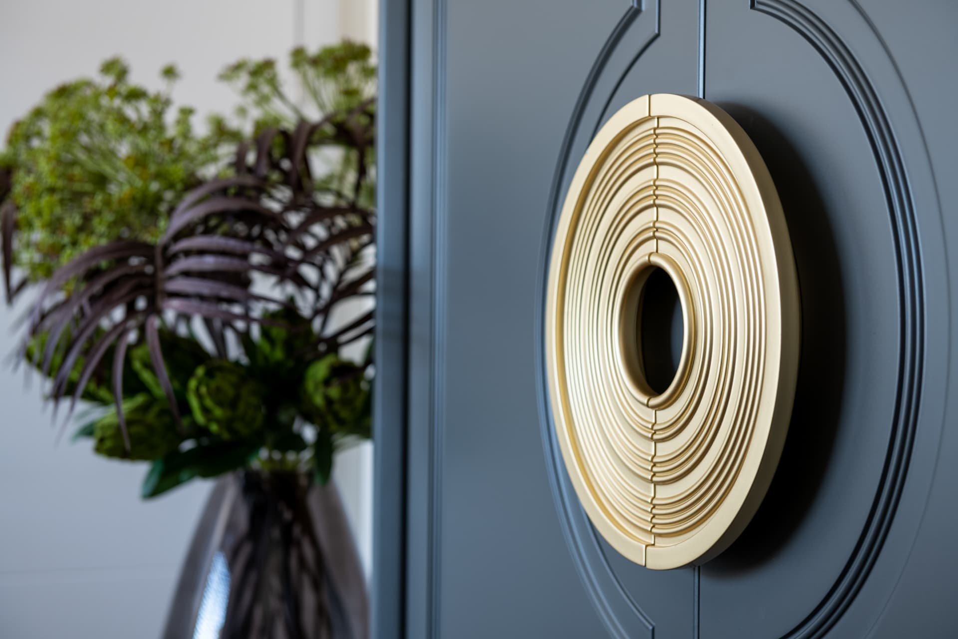 Brass ring-shaped door handle with concentric grooves on a dark grey paneled door in Emperador Dark
