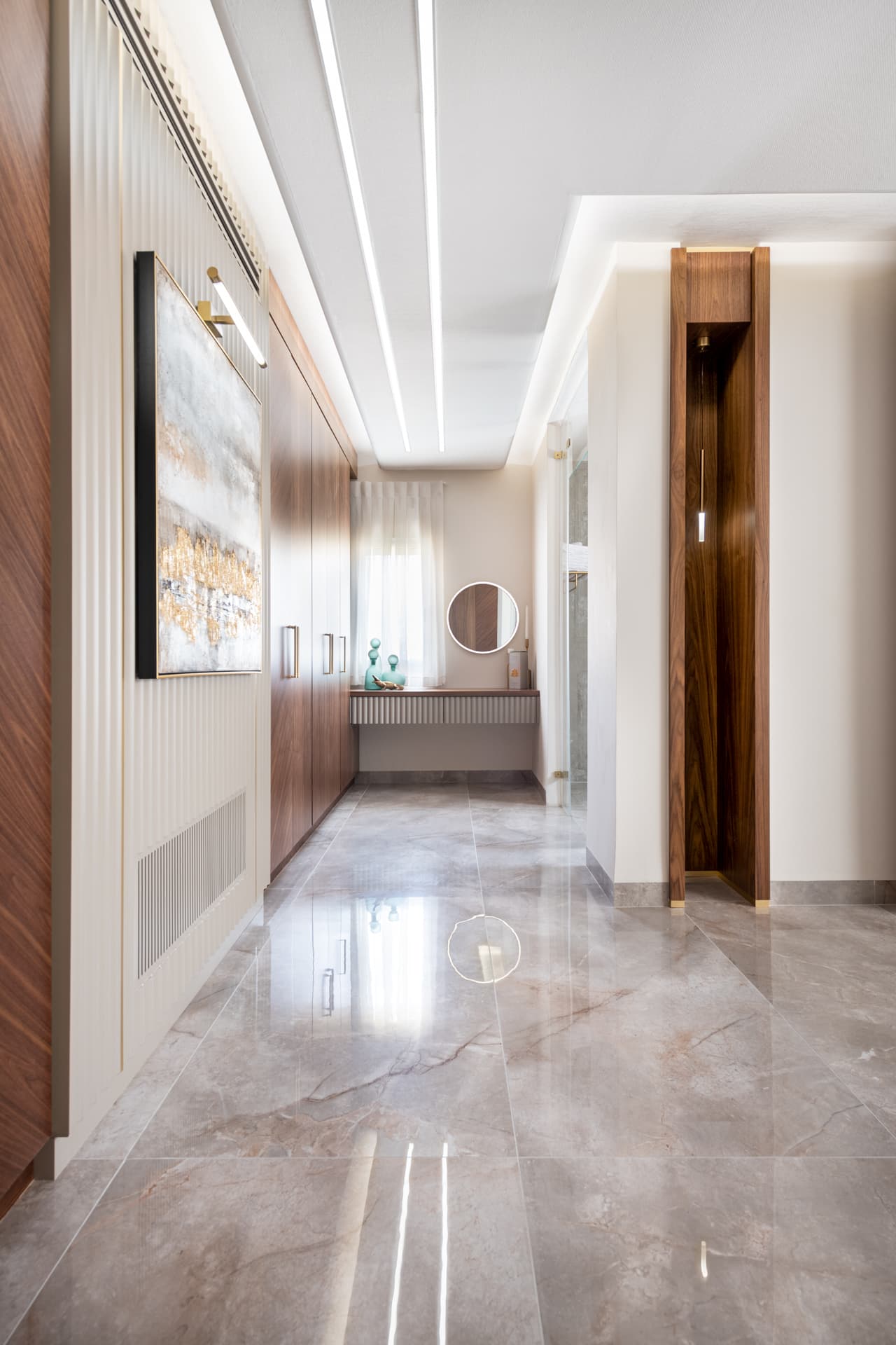 Walnut wardrobe corridor beneath linear ceiling light slots, with a tall walnut recess opposite, in the master bedroom of Emperador Dark