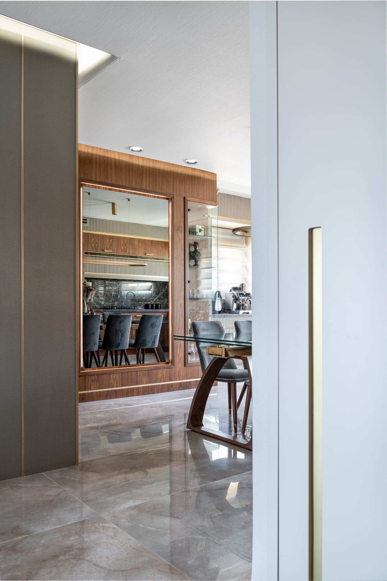 Brass-inlaid grey panels and a white door with a long brass pull frame a view of the walnut dining wall in the entrance of Emperador Dark