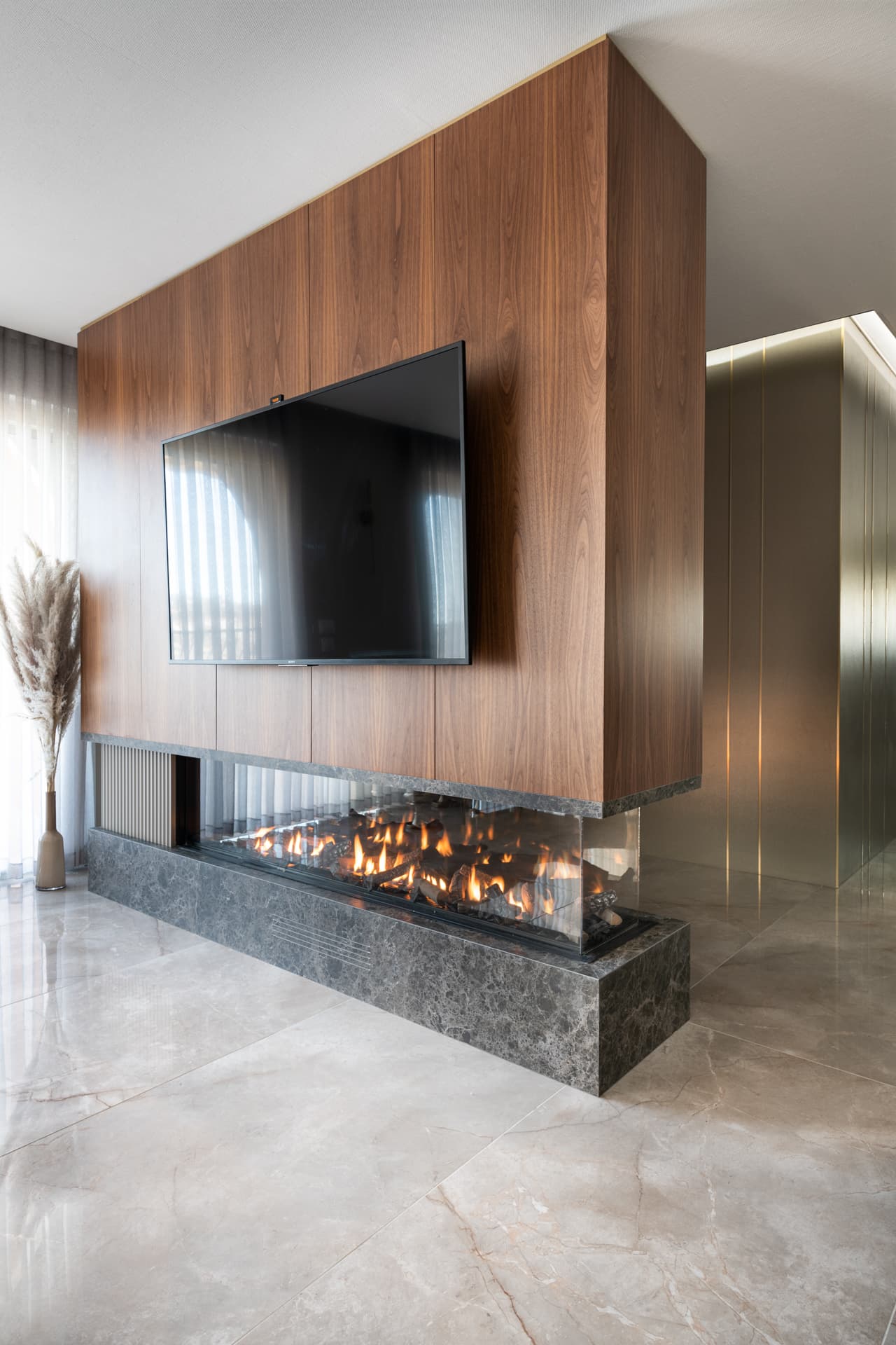 Angled view of the freestanding walnut fireplace wall on a dark veined stone base in the living room of Emperador Dark