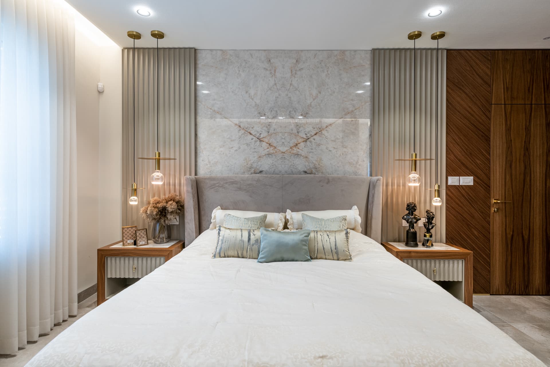 Wingback headboard against a veined stone panel flanked by fluted walls and brass pendants in the master bedroom of Emperador Dark