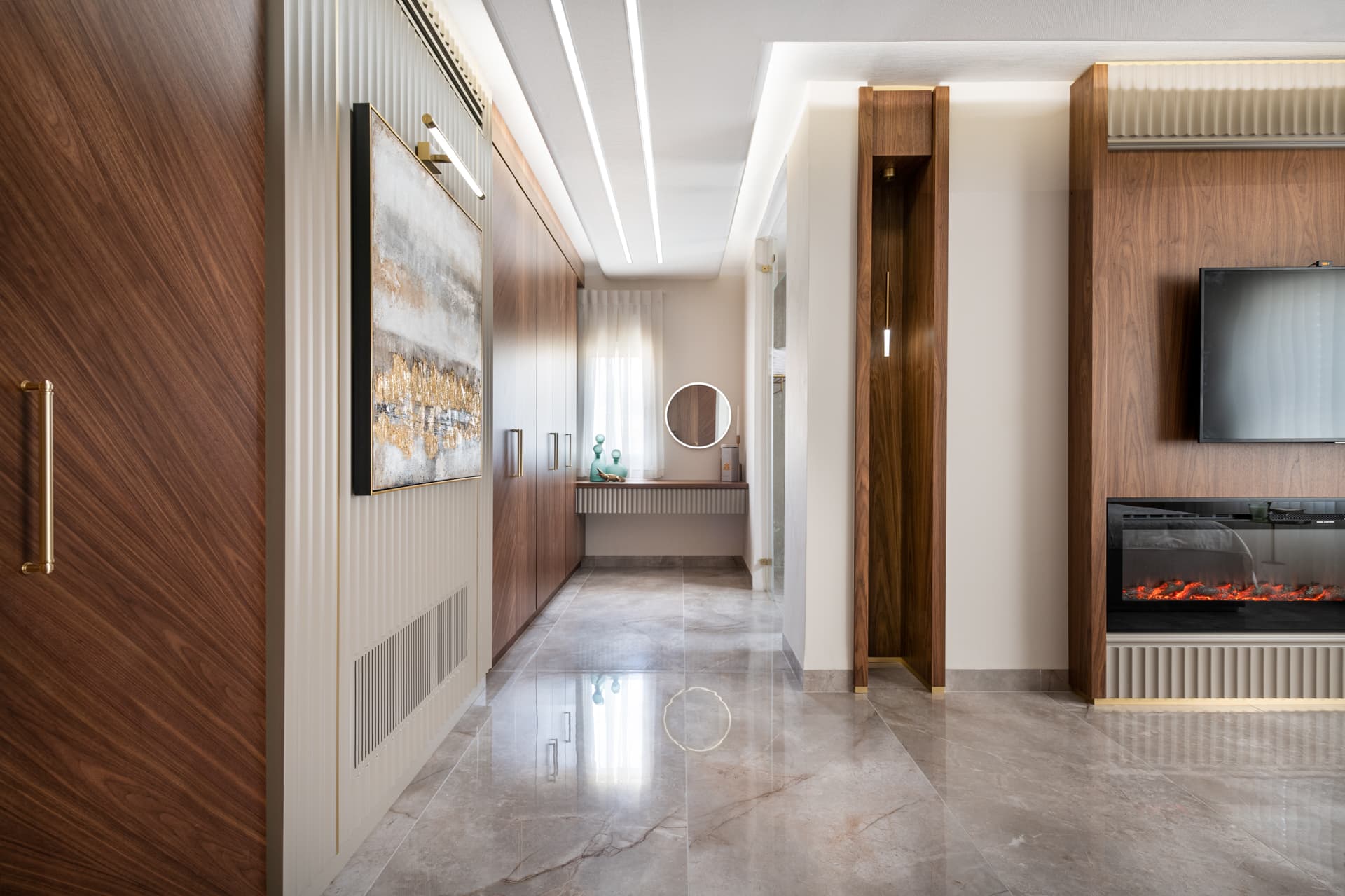 Corridor of walnut wardrobes leading to a vanity nook with a round mirror in the master bedroom of Emperador Dark