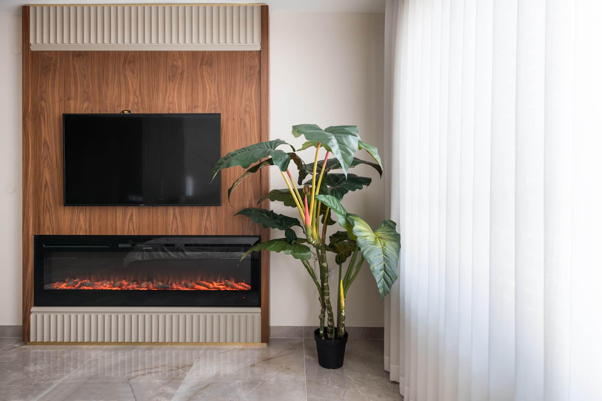 Walnut media wall with a wide electric fireplace framed by fluted panels beside sheer curtains in the master bedroom of Emperador Dark