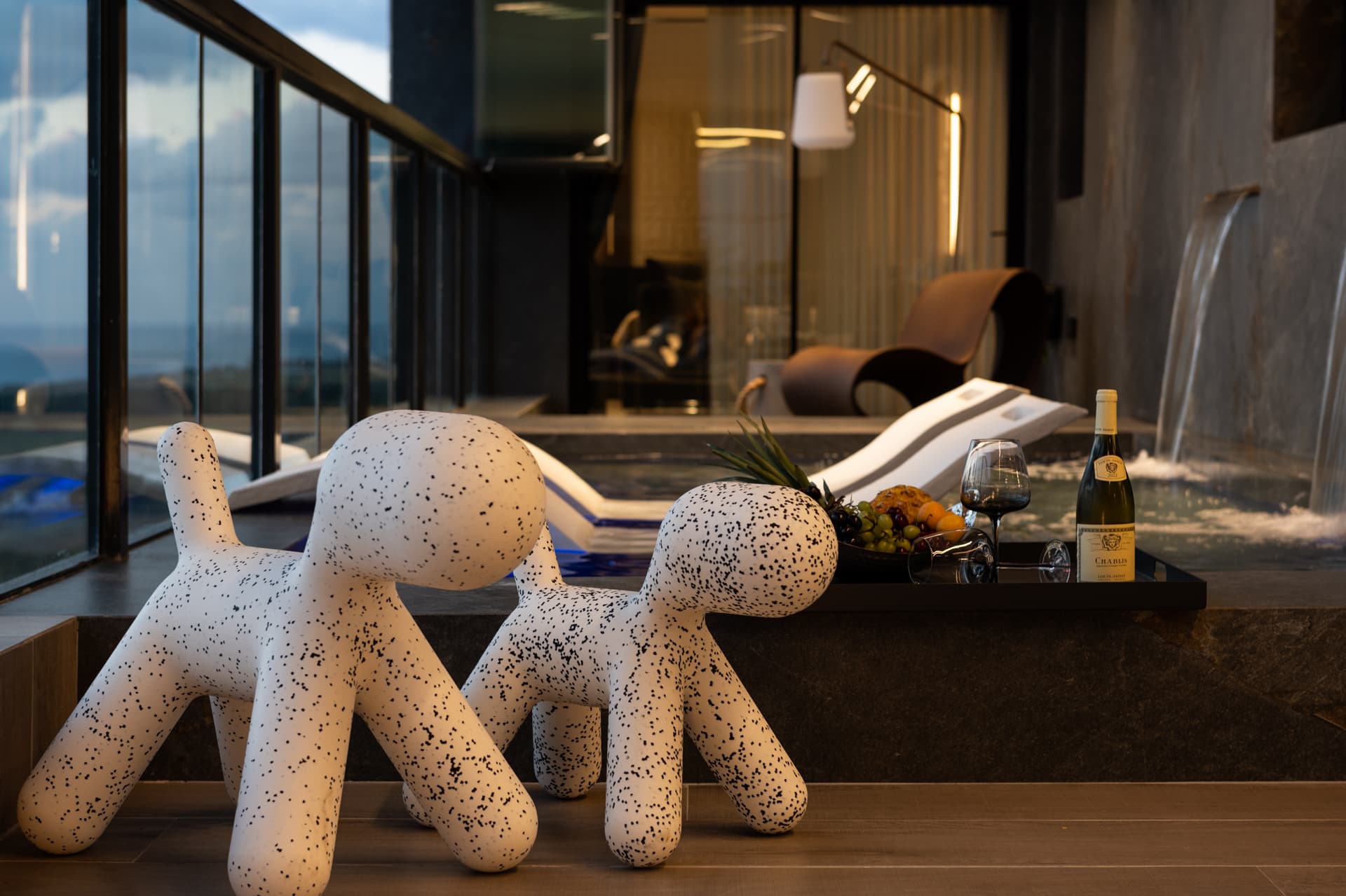 Pair of speckled dog-shaped sculptures on the wood deck beside the pool with white loungers and waterfalls in Khayyal
