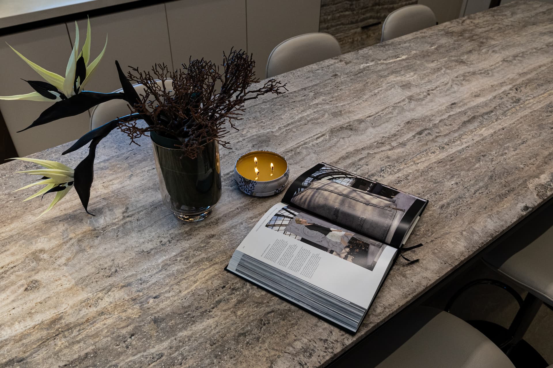 Veined stone island top with a vase of branches, lit candle and open book beside bar stools in the kitchen of Khayyal
