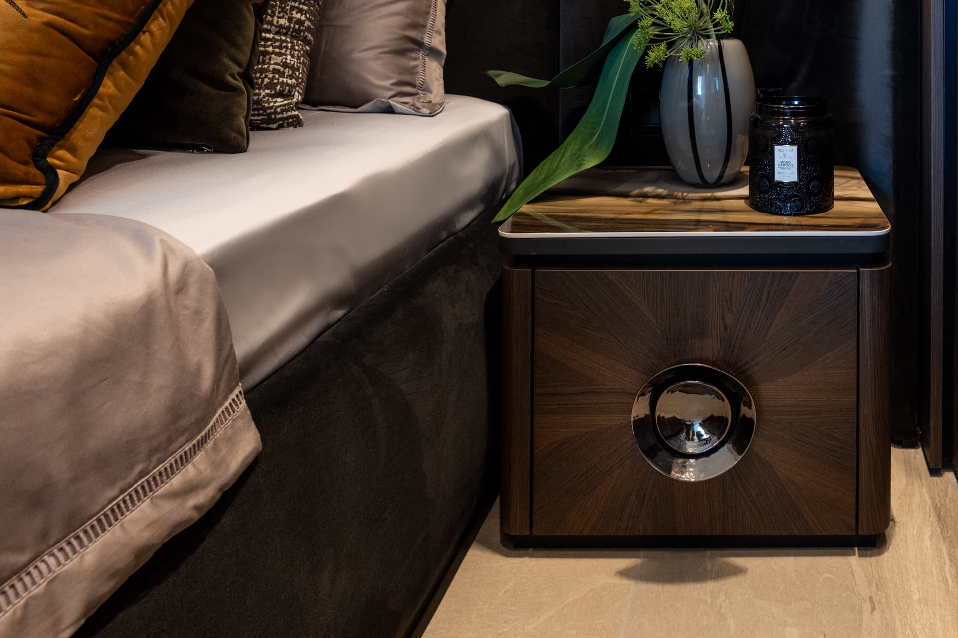 Wider view of the sunburst walnut nightstand beside the bed with satin linens in the master bedroom of Khayyal