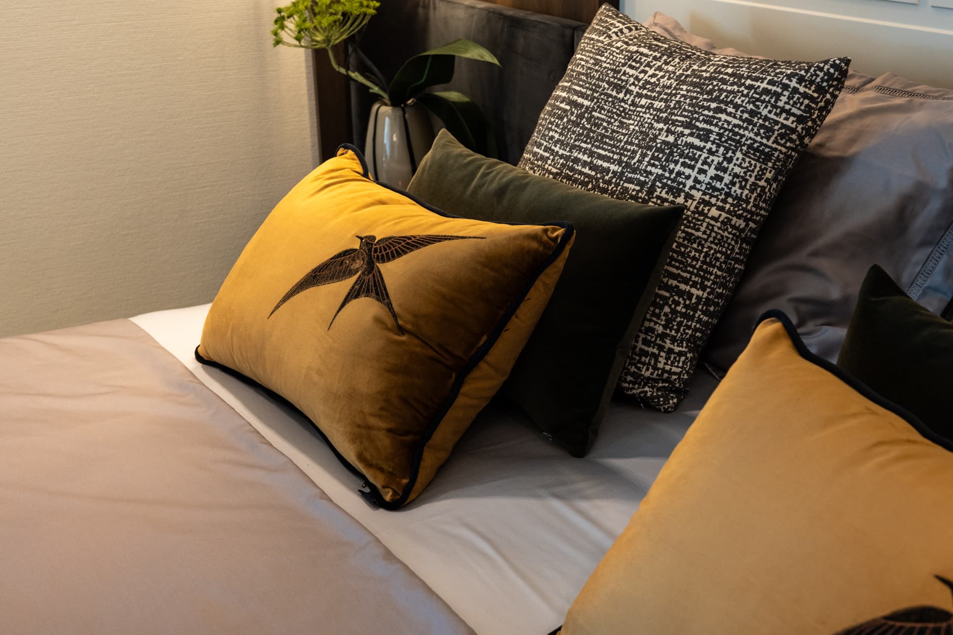 Ochre velvet cushions with an embroidered swallow motif among textured pillows on the bed in the master bedroom of Khayyal