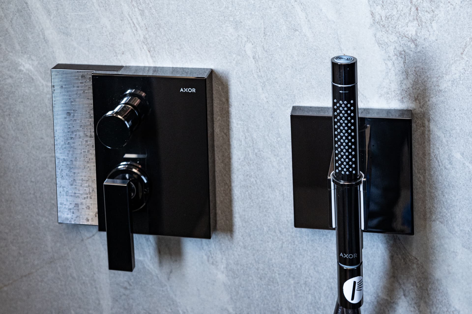 Black shower mixer and slim hand shower mounted on grey stone-look tiles in the master bathroom of Khayyal