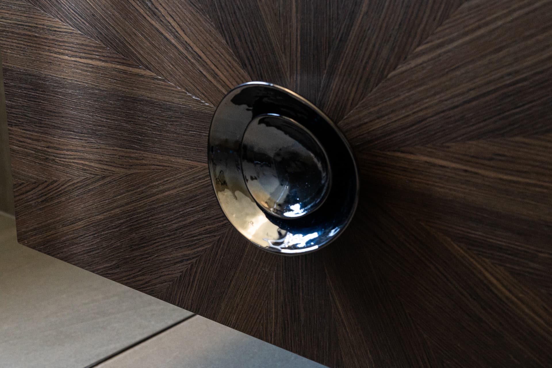 Glossy dark round pull set into radiating sunburst wood veneer on a cabinet front in Khayyal