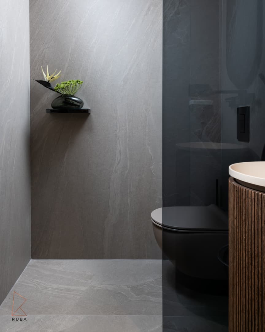 Guest toilet with grey stone-look walls, a floating flower shelf and the edge of a fluted wood basin column in Khayyal