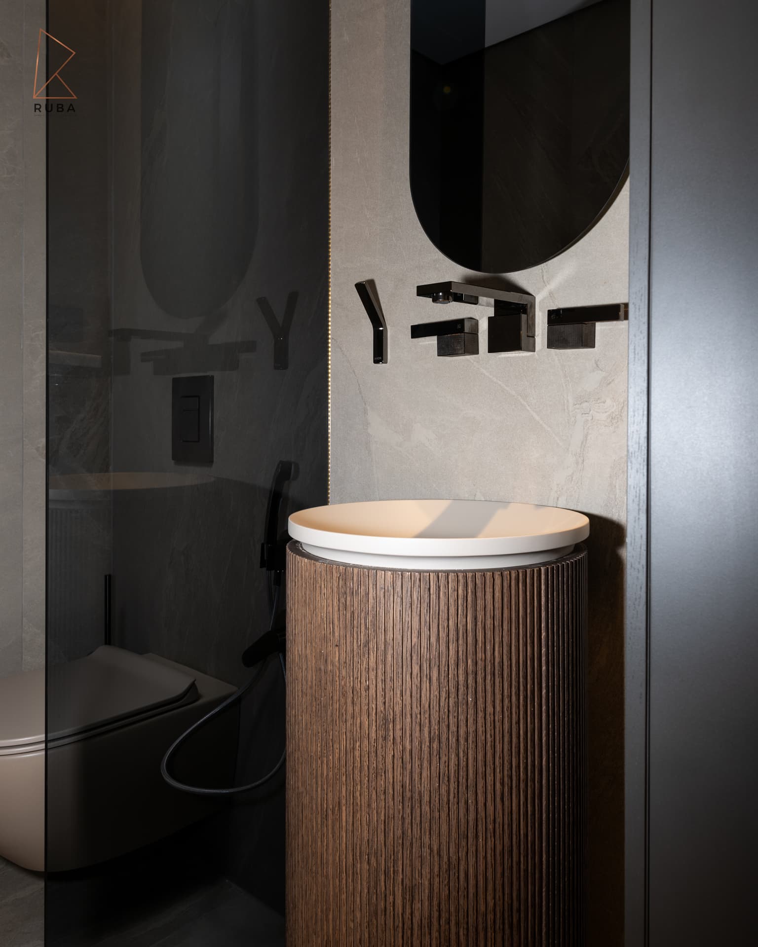 Fluted wood pedestal basin with black wall taps under a round smoked mirror in the guest toilet of Khayyal