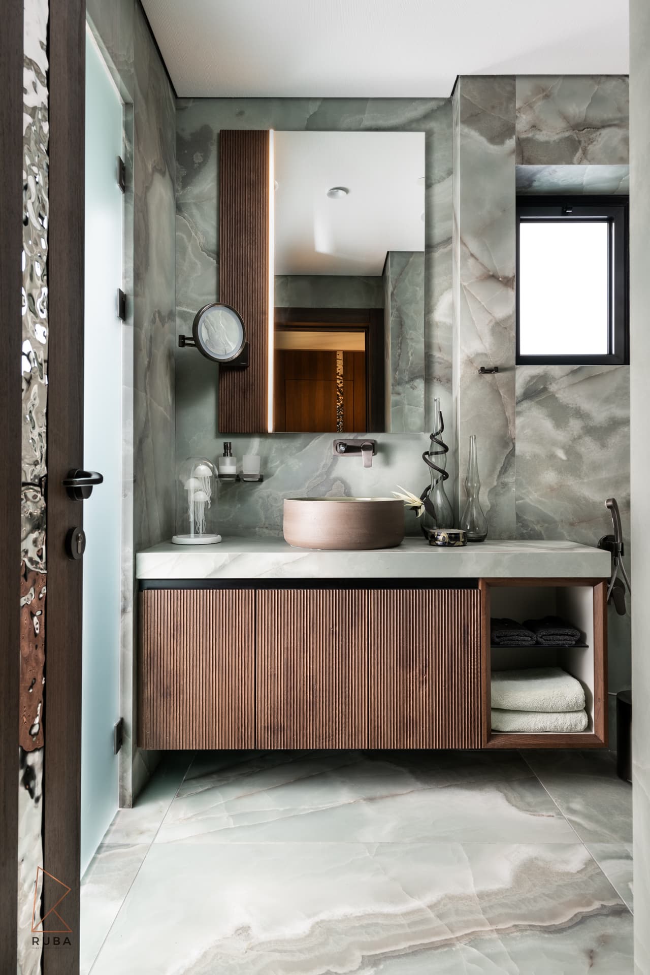 Kids bathroom clad in green onyx-look stone with a fluted wood vanity, terracotta vessel basin and backlit mirror in Khayyal