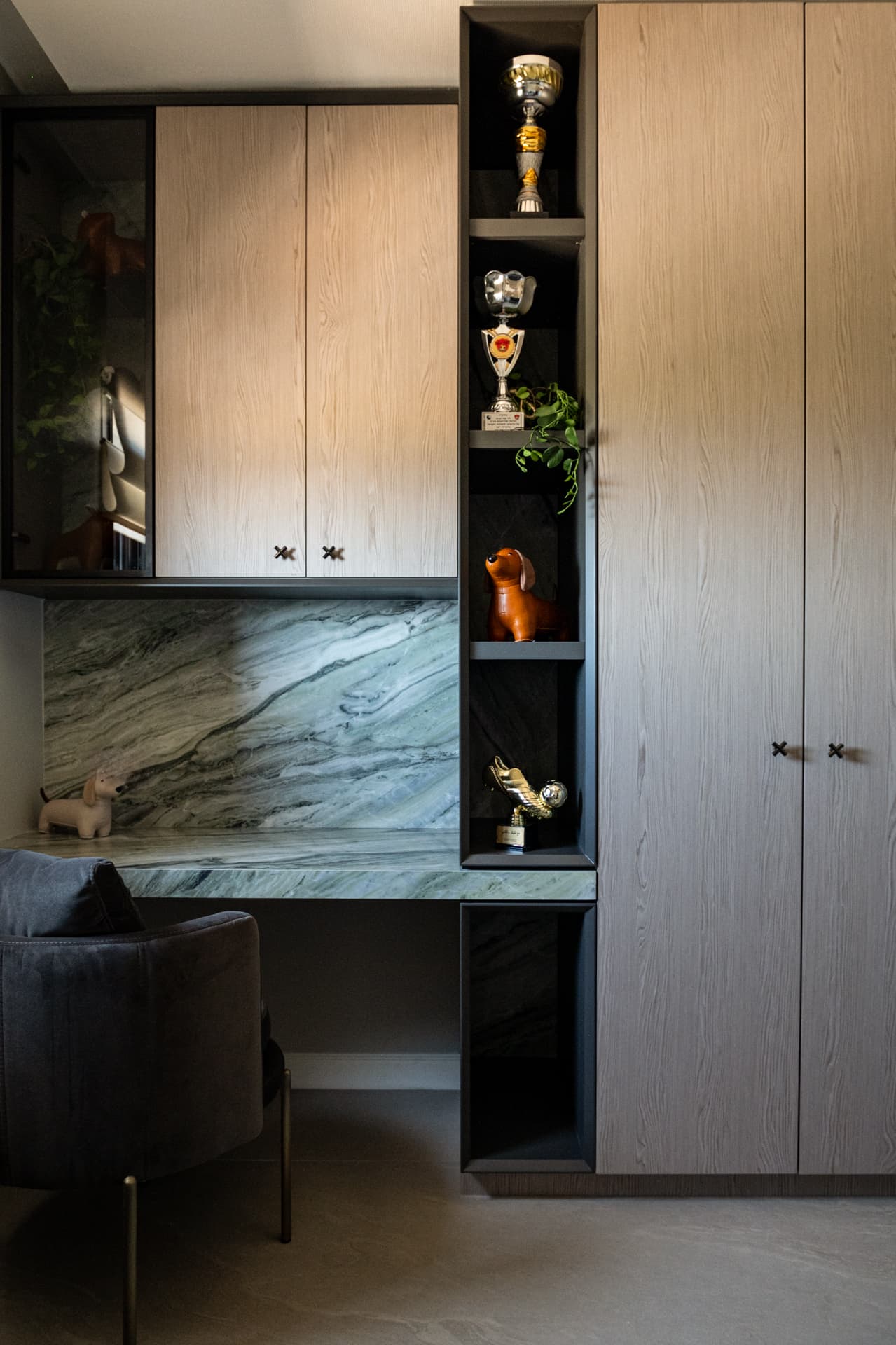 Wall of wood wardrobes with a black open display column and green veined stone desk in a kids room of Khayyal