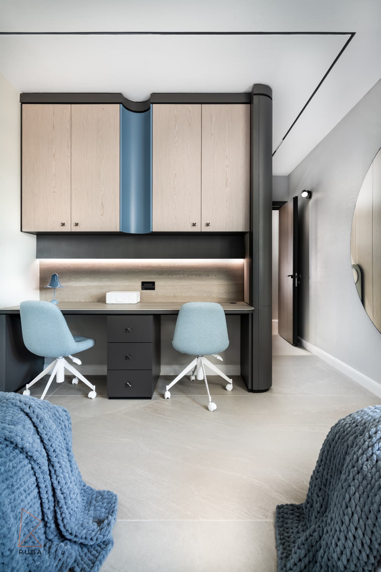 Double study desk with two blue chairs under wood cabinets with a curved blue channel in a kids room of Khayyal