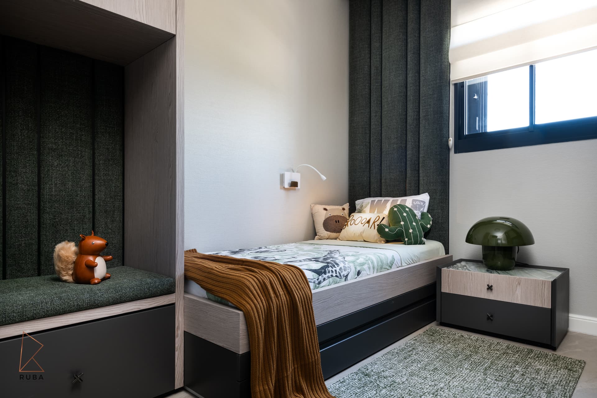 Cushioned window-seat niche beside a bed with an ochre knit throw and green mushroom lamp in a kids room of Khayyal