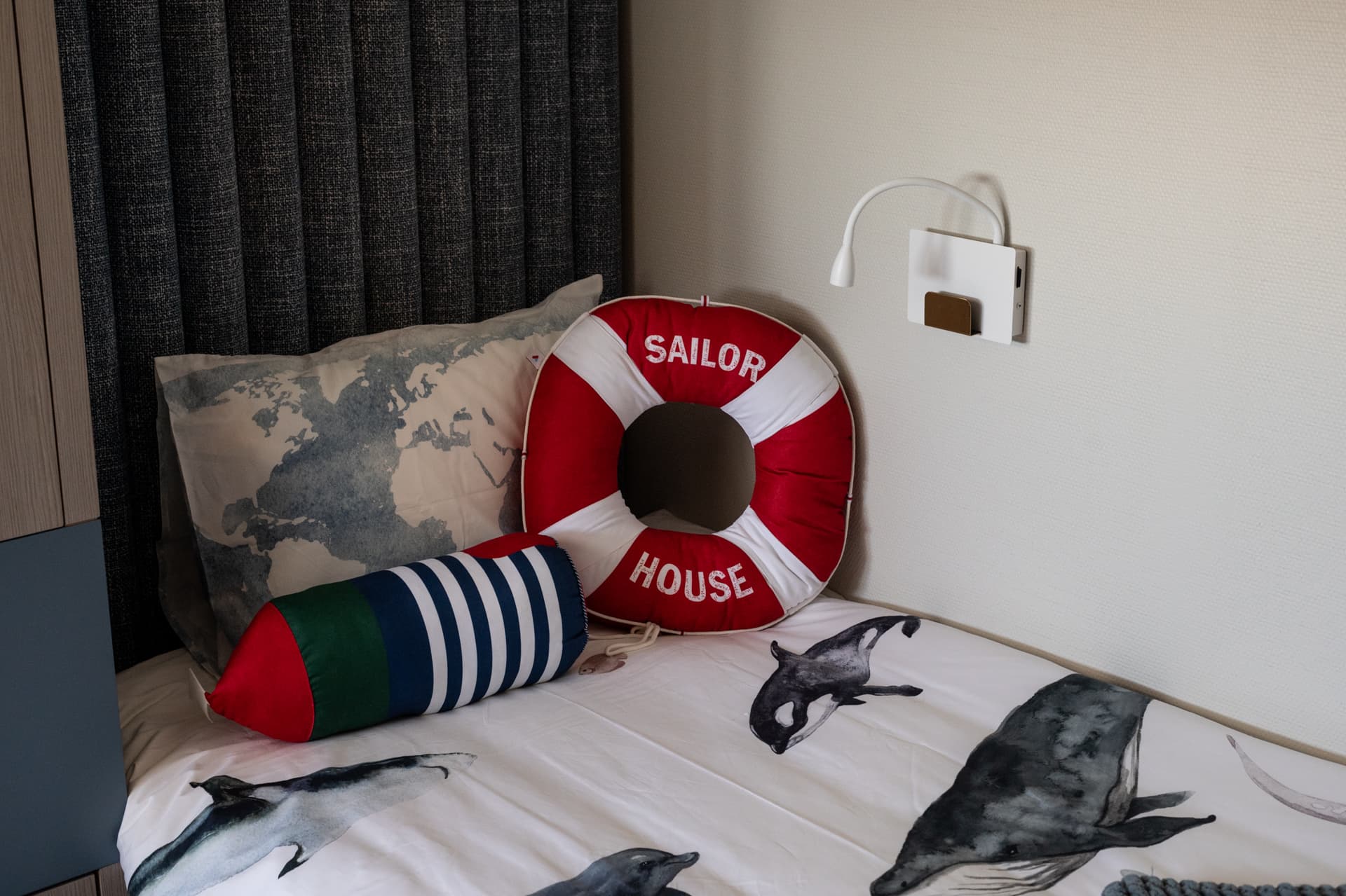 Close view of a bed with a life-ring cushion, striped bolster and whale-print bedding in a kids room of Khayyal