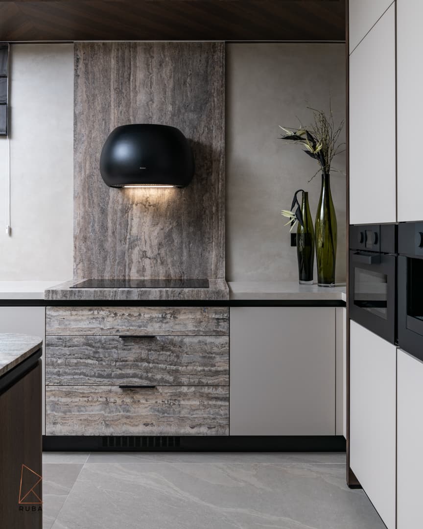 Black dome range hood on a veined stone backsplash above an induction hob and stone-clad drawers in the kitchen of Khayyal