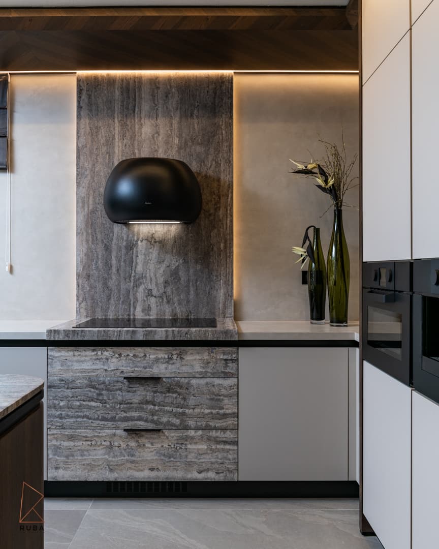 Backlit veined stone backsplash with a black dome hood and warm cove lighting over the cooktop in the kitchen of Khayyal