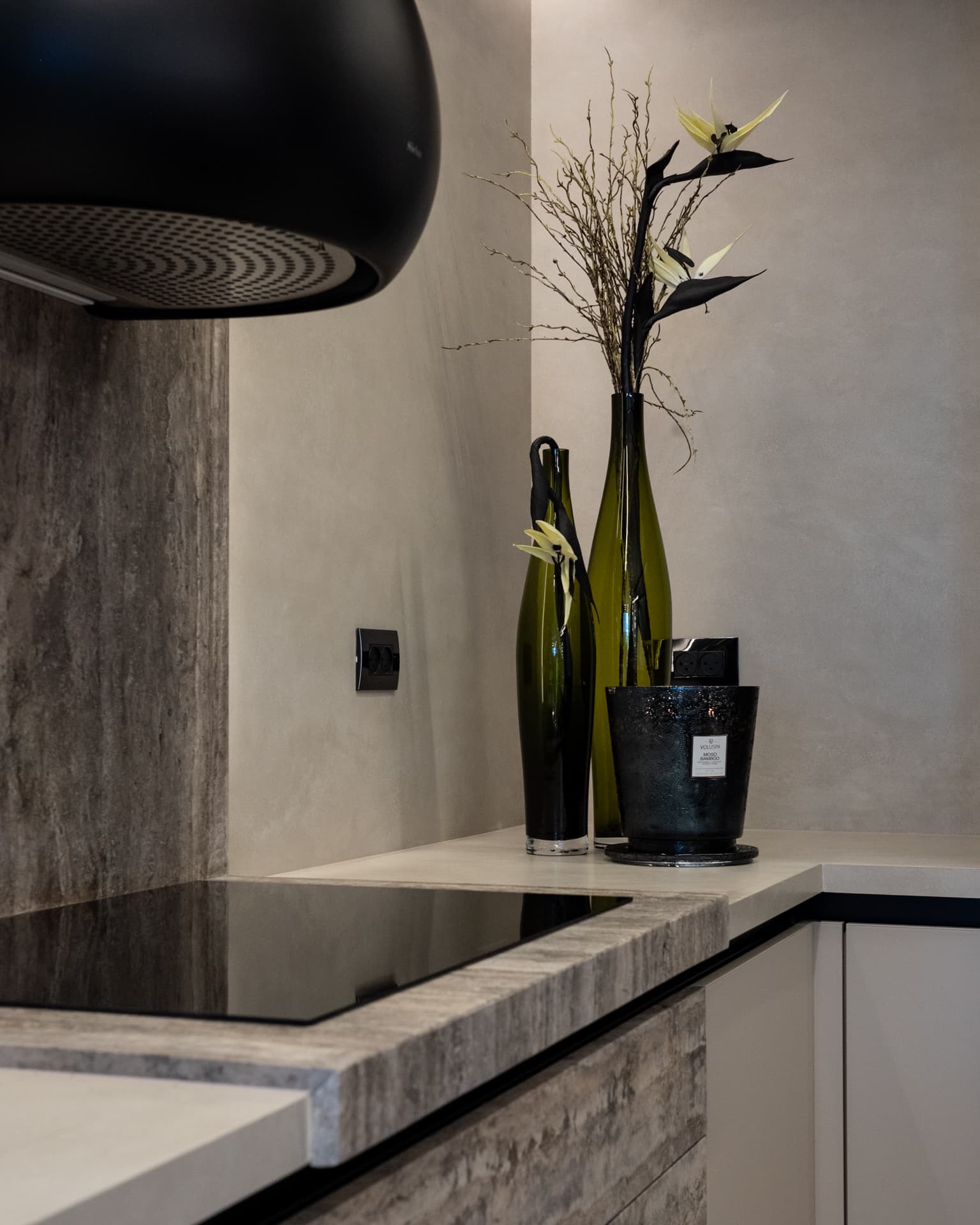 Close view of a veined stone countertop edge beside an induction hob, under a black dome hood in the kitchen of Khayyal