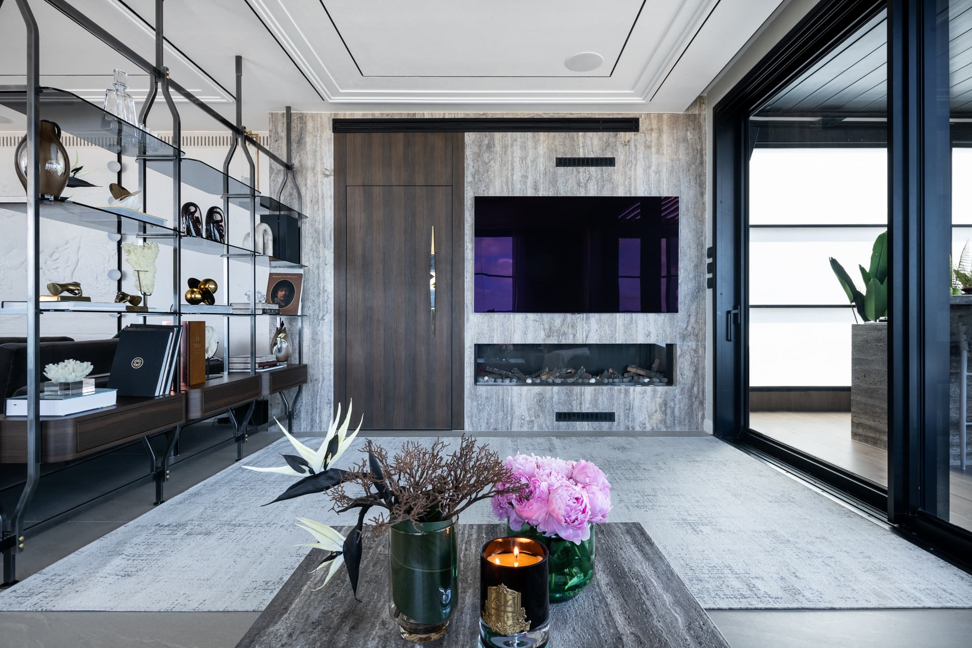 Veined stone media wall with a linear fireplace, walnut door and suspended metal shelving in the living room of Khayyal