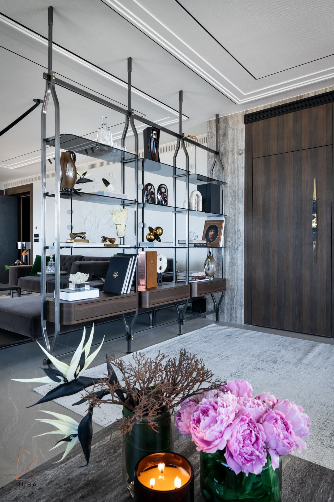 Ceiling-hung metal and glass shelving with sculptural objects beside a walnut door in the living room of Khayyal