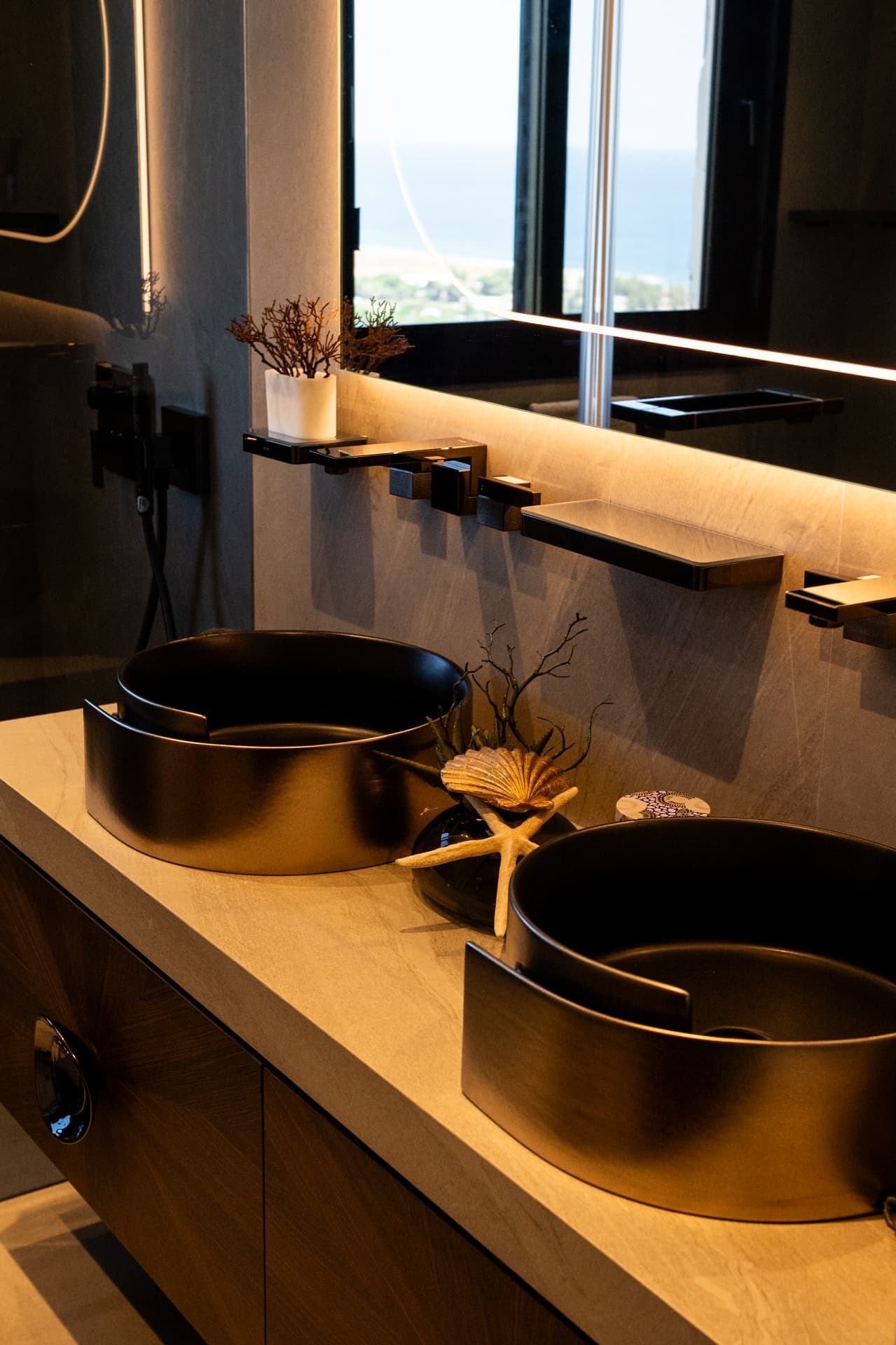 Two dark metallic vessel basins with wall-mounted black taps and a sea-view window in the master bathroom of Khayyal